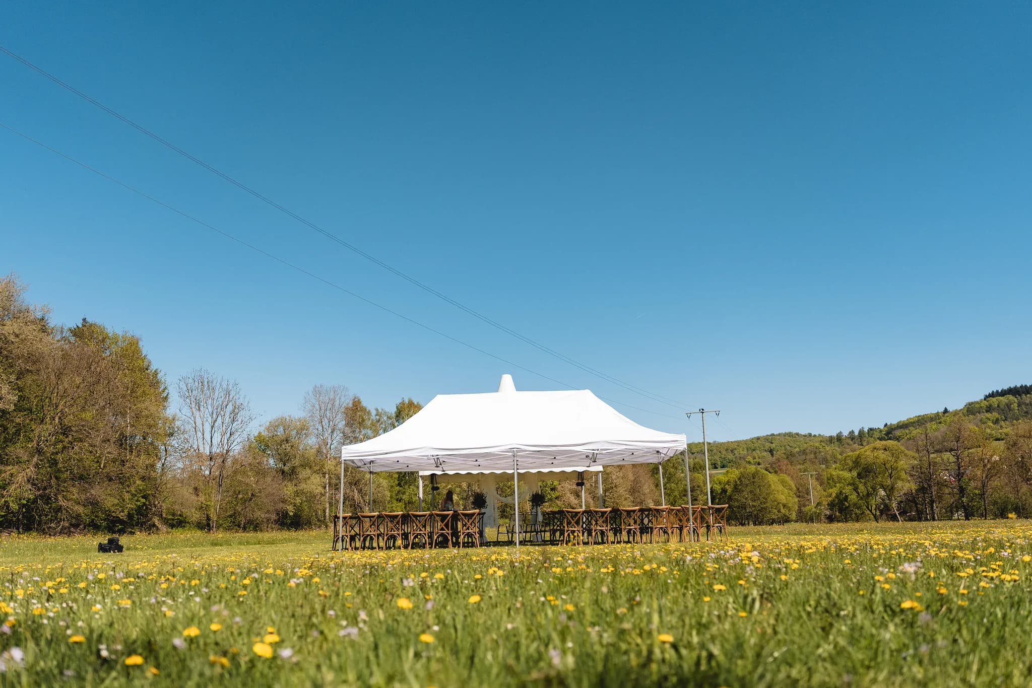 Weißes Festzelt für eine freie Trauung auf einer blühenden Wiese vor der Kulisse der Rhön an einem sonnigen Maitag.