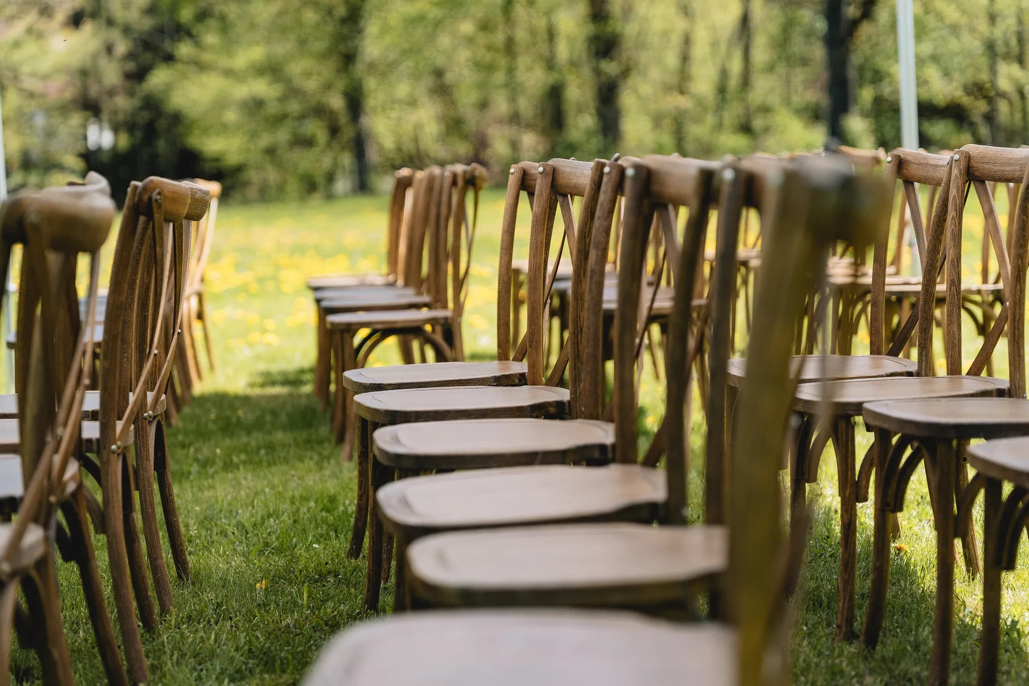 Reihen hölzerner Stühle stehen für eine freie Trauung auf der saftig grünen Wiese einer Hochzeit in der Rhön.
