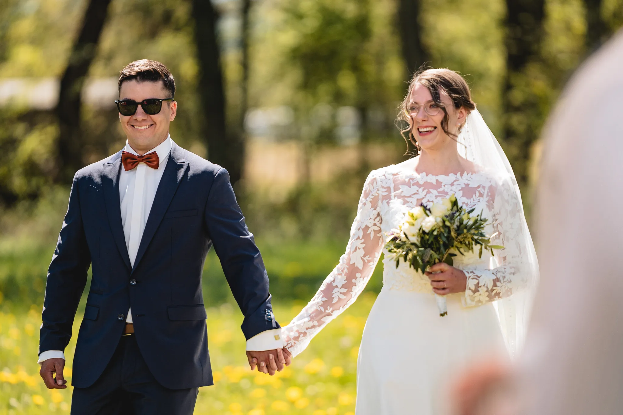 Stefanie und Ralf halten sich glücklich an den Händen bei ihrer freien Trauung auf einer grünen Wiese in der Rhön.
