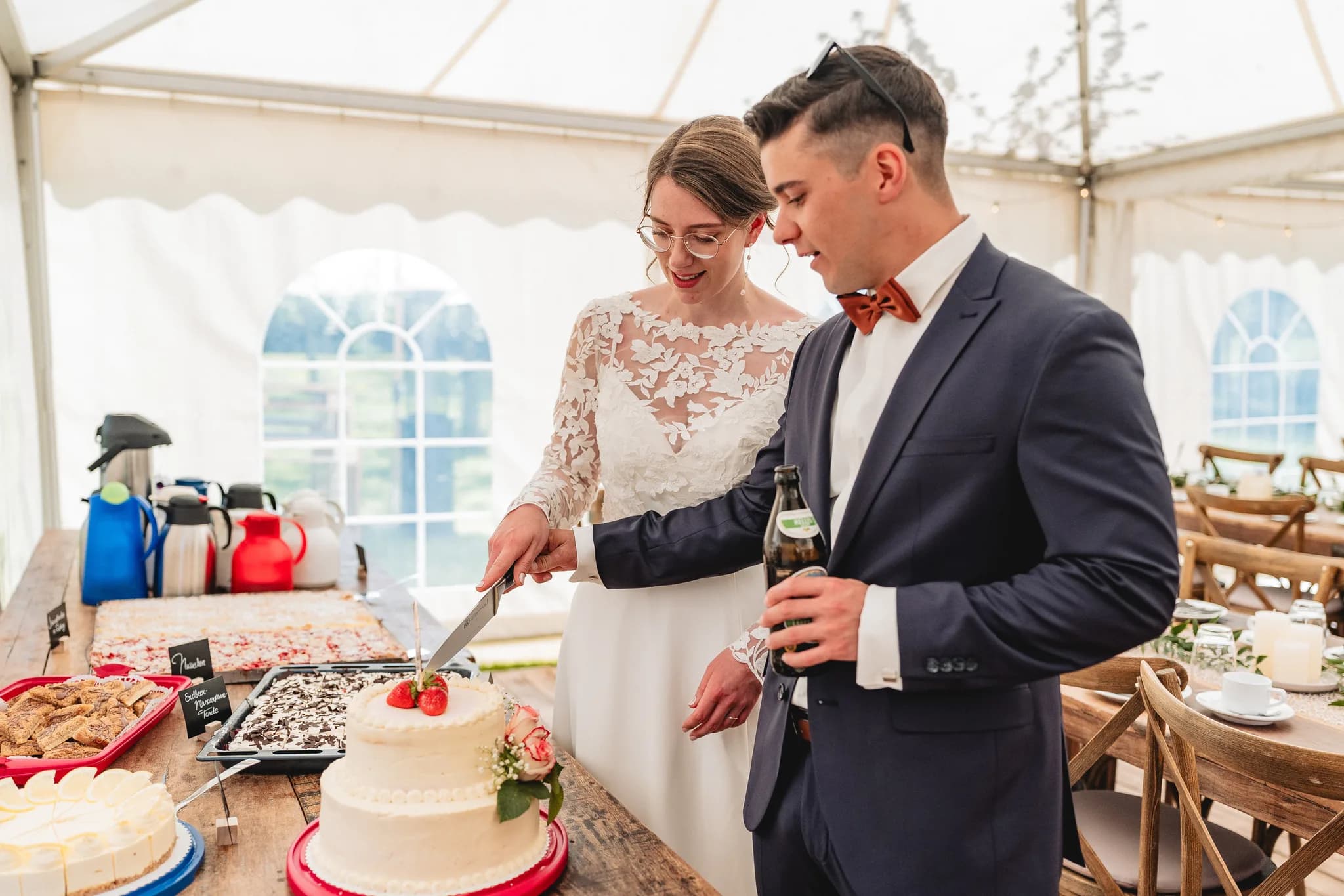 Stefanie und Ralf schneiden gemeinsam die Hochzeitstorte im hellen Festzelt bei ihrer Gartenhochzeit in der Rhön.