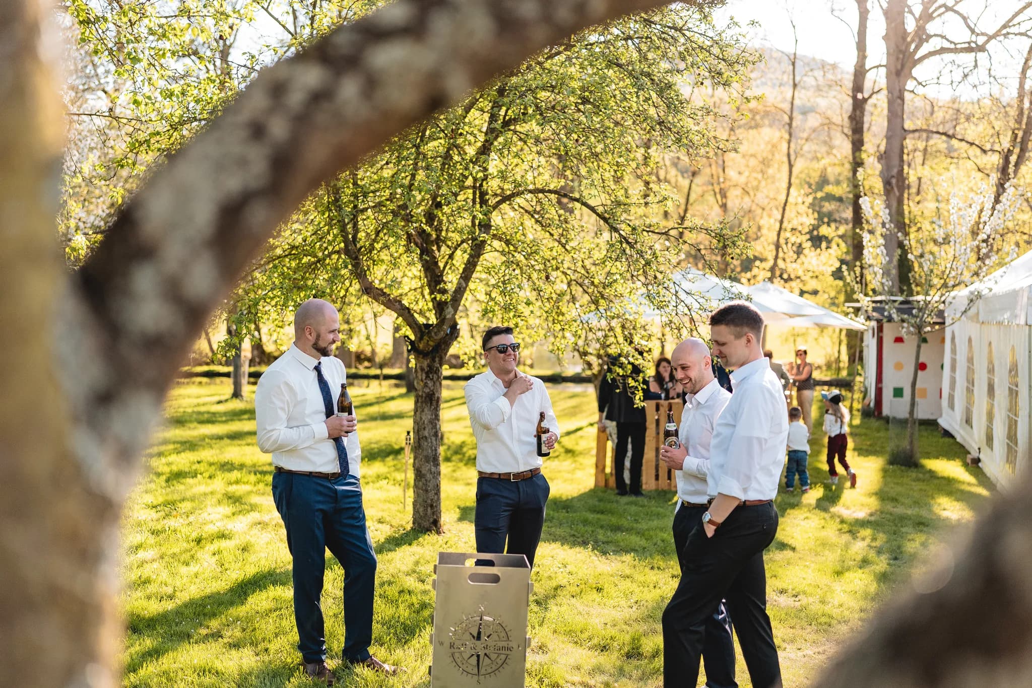 Hochzeitsgäste unterhalten sich entspannt mit Bierflaschen im sonnigen Garten der Ulstermühle in der Rhön.