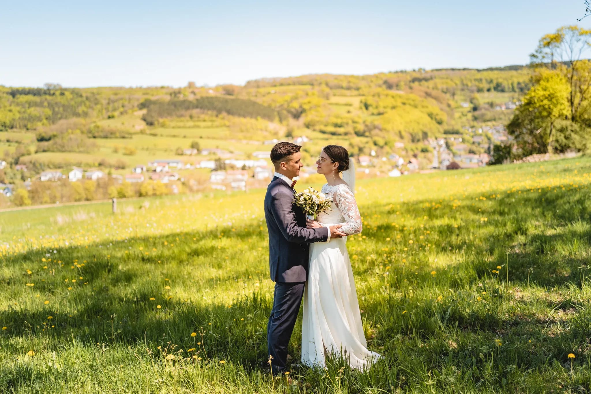 Stefanie und Ralf blicken sich bei sonnigem Frühlingswetter liebevoll auf einer grünen Wiese in der Rhön an.