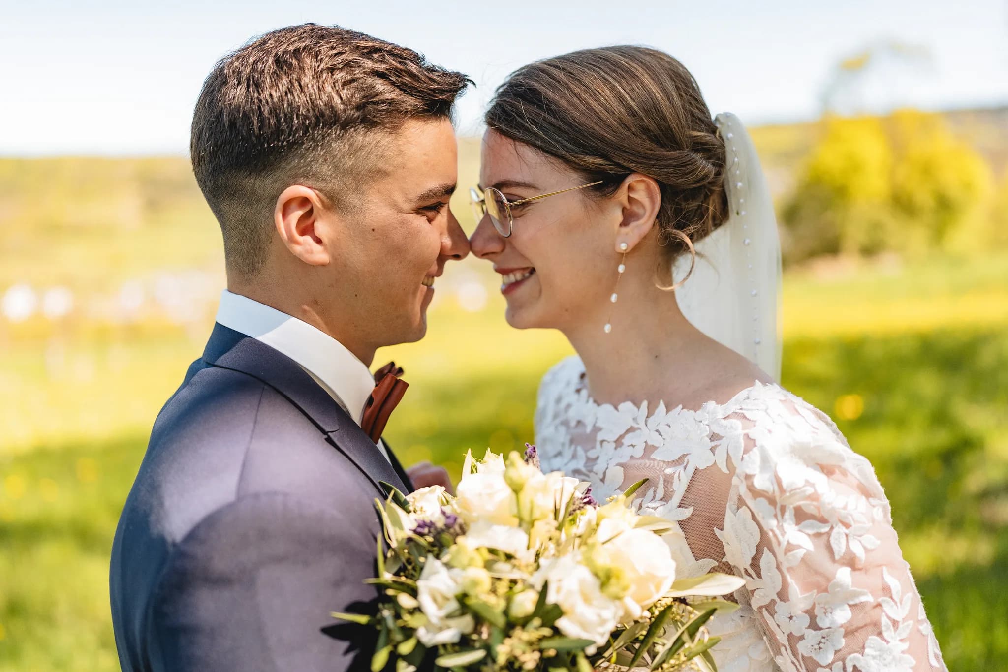 Stefanie und Ralf berühren sich zärtlich mit den Stirnen auf einer grünen Frühlingswiese bei ihrer Hochzeit in der Rhön.