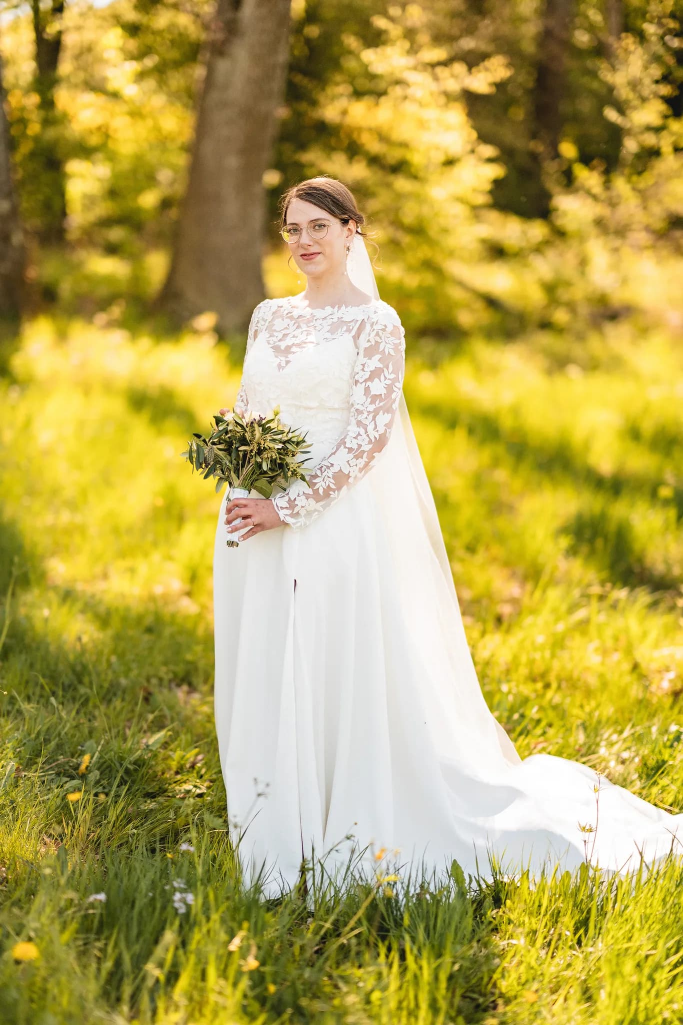 Braut Stefanie mit Hochzeitsstrauß und langem Schleier inmitten einer sonnigen grünen Wiese vor der Kulisse der Rhön.