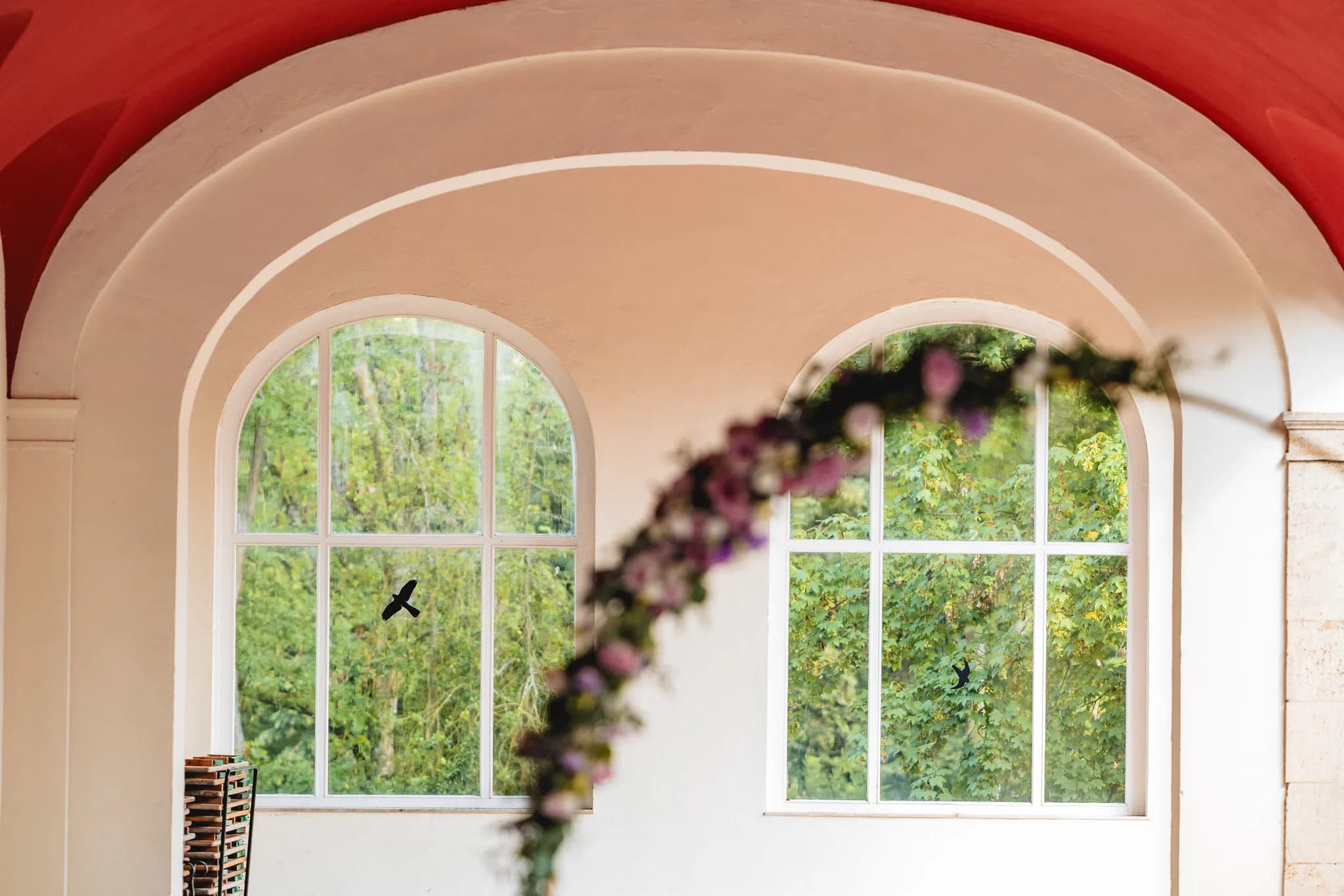 Blick durch einen Blumenbogen auf zwei große Rundbogenfenster im Dolce by Wyndham Bad Nauheim mit grüner Parkaussicht.