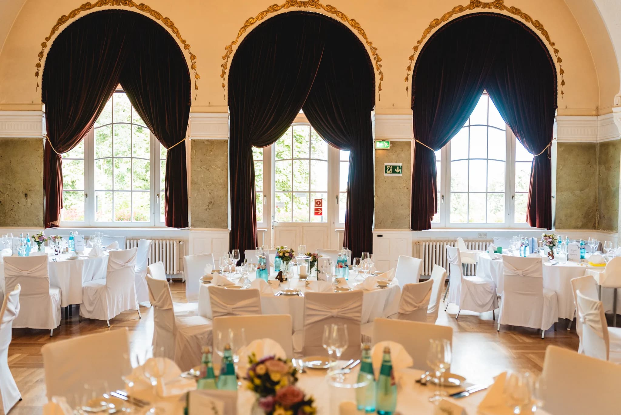 Festlich eingedeckte Hochzeitstische mit weißen Hussen in einem eleganten Saal des Dolce by Wyndham Bad Nauheim.