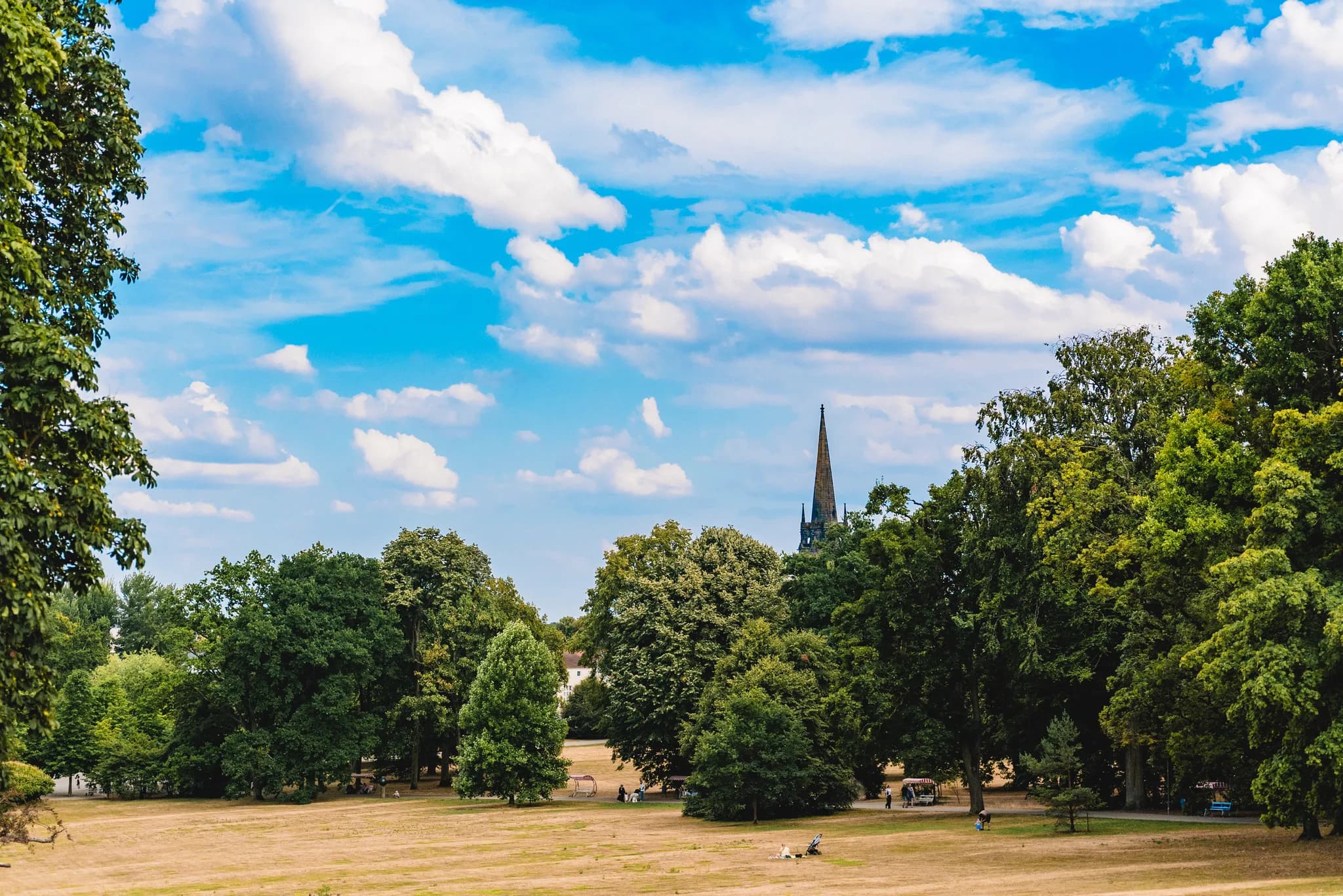 Blick auf die sonnige Parklandschaft beim Dolce by Wyndham Bad Nauheim mit der Turmspitze im Hintergrund.
