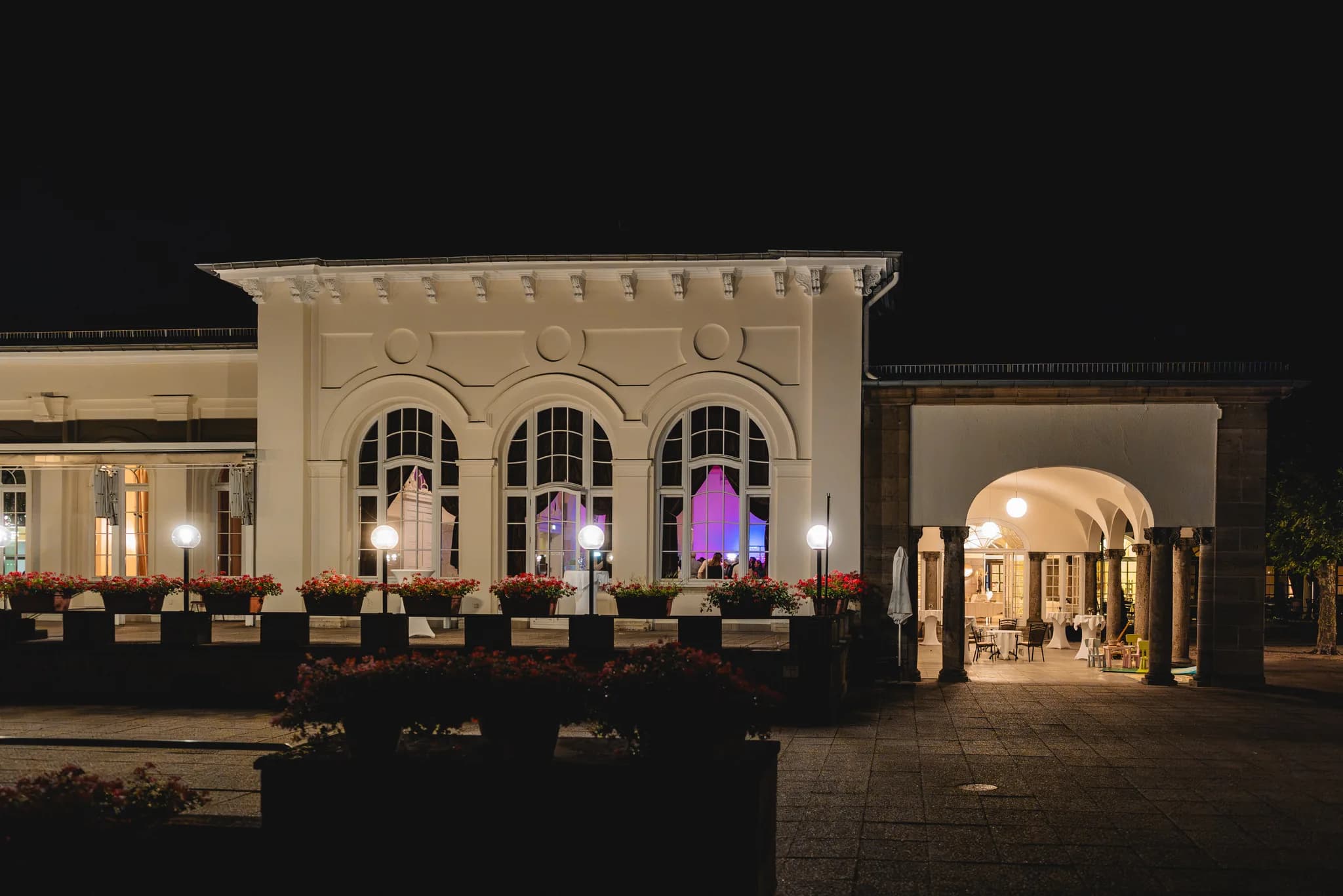 Die beleuchtete Fassade des Dolce by Wyndham Bad Nauheim bei Nacht mit Blick auf die festlich geschmückten Innenräume.
