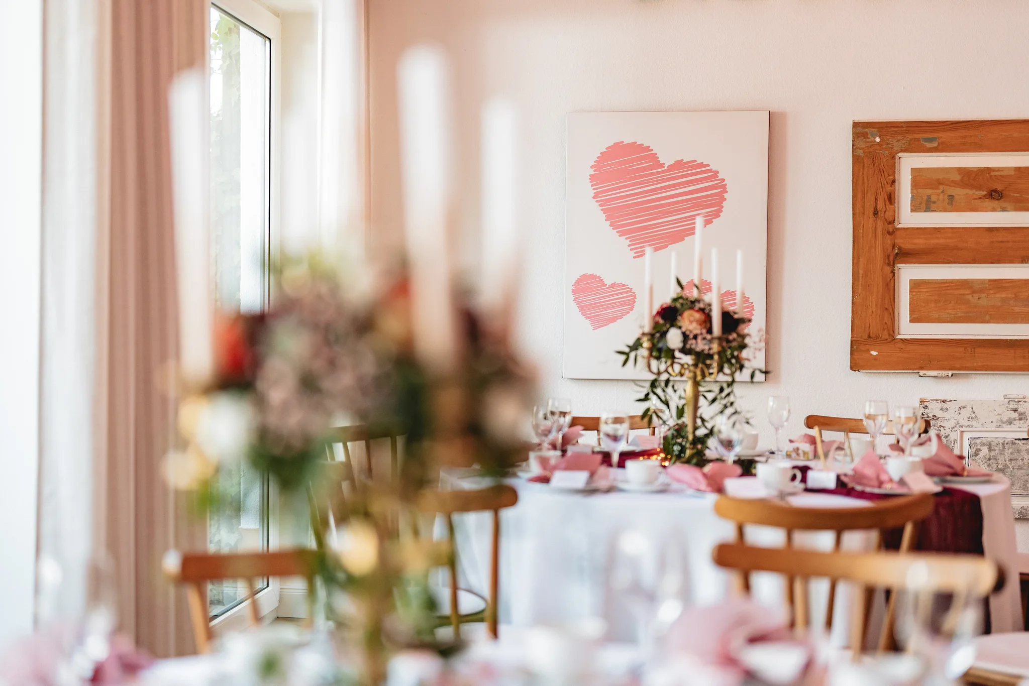Festlich gedeckte Hochzeitstafeln mit Blumenschmuck und einem Herzbild an der Wand in einem Raum in Hofbieber.