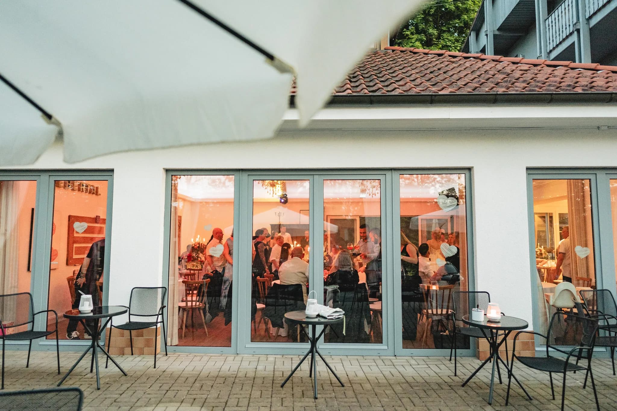 Gäste bei der Hochzeitsfeier im hell erleuchteten Innenraum einer Location in Hofbieber gesehen von der Terrasse aus.