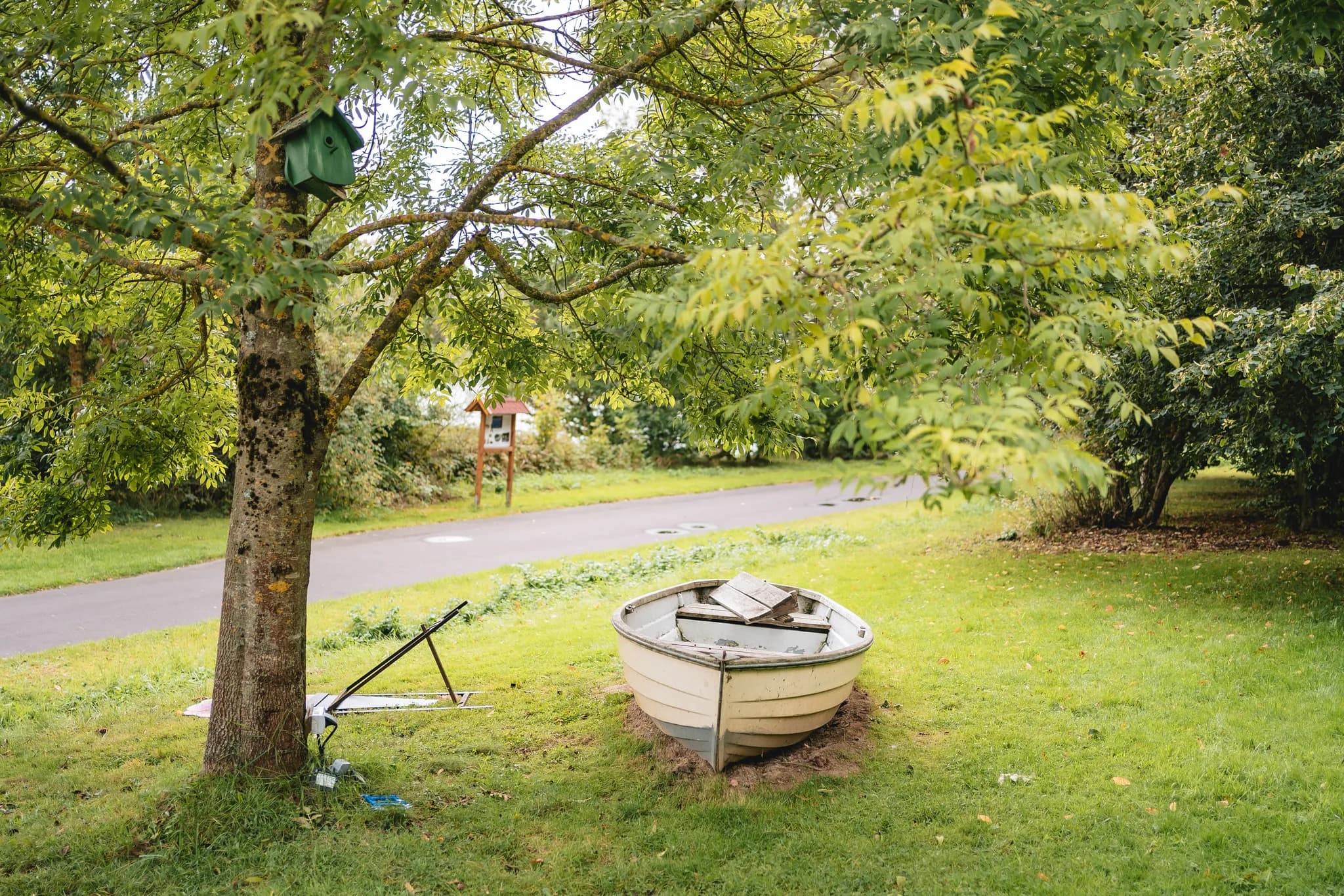 Ein beigefarbenes Ruderboot steht idyllisch auf der grünen Wiese vor dem Baum am Lakeside Resort Michaela.