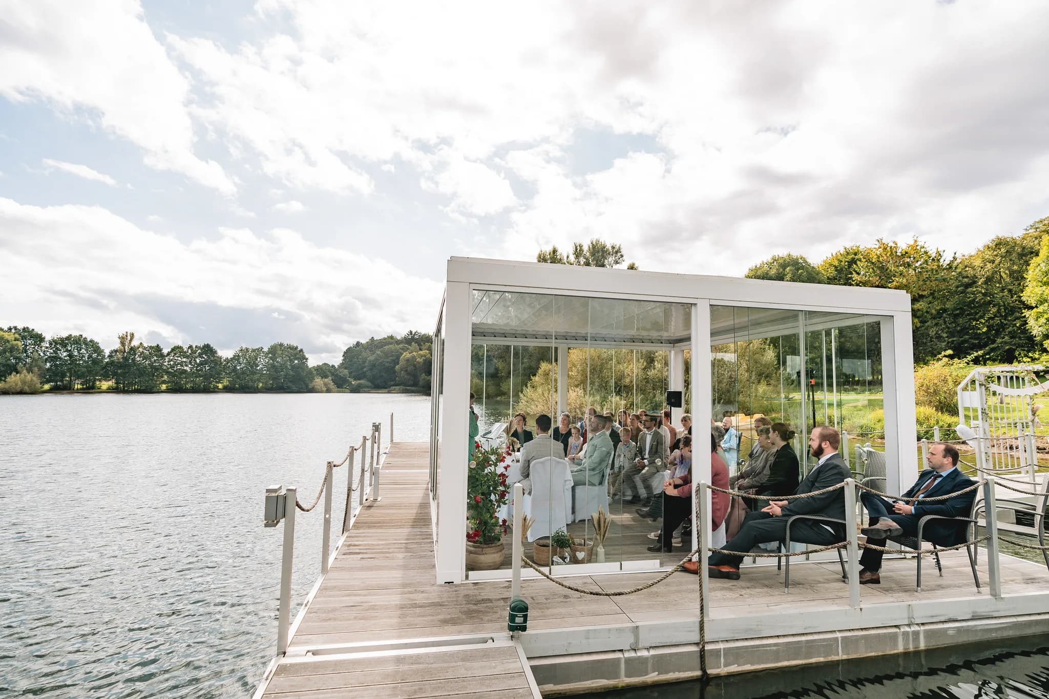 Hochzeitsgesellschaft bei einer Zeremonie im gläsernen Pavillon direkt am See des Lakeside Resorts Michaela.