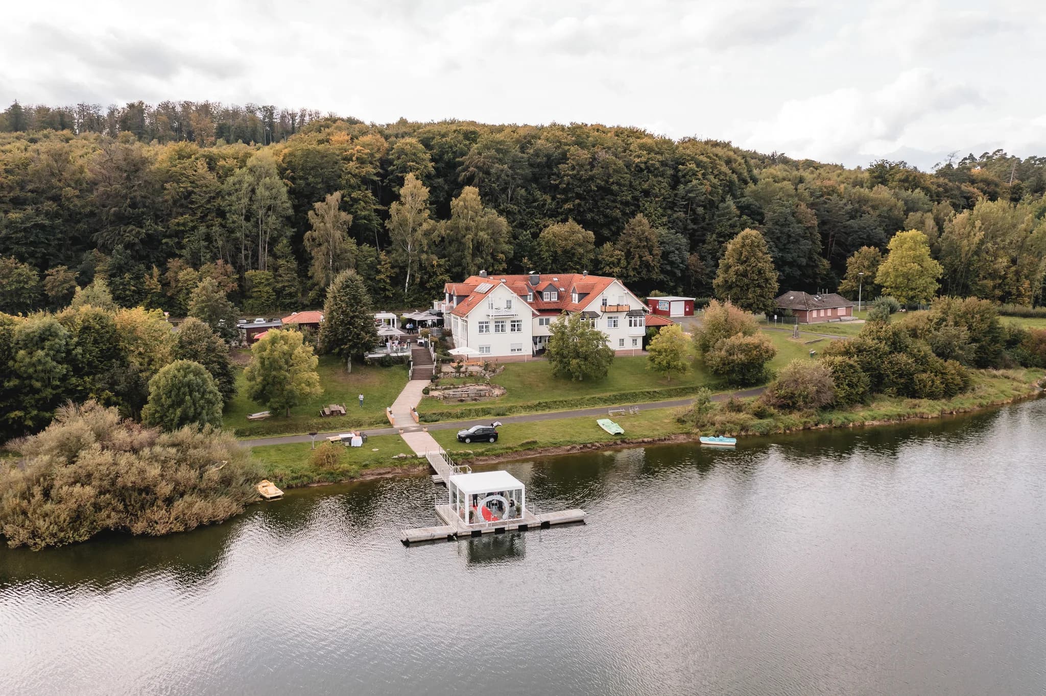 Luftaufnahme vom Lakeside Resort Michaela mit weißem Gebäude, weitläufigem Waldgrundstück und einem Steg am See.