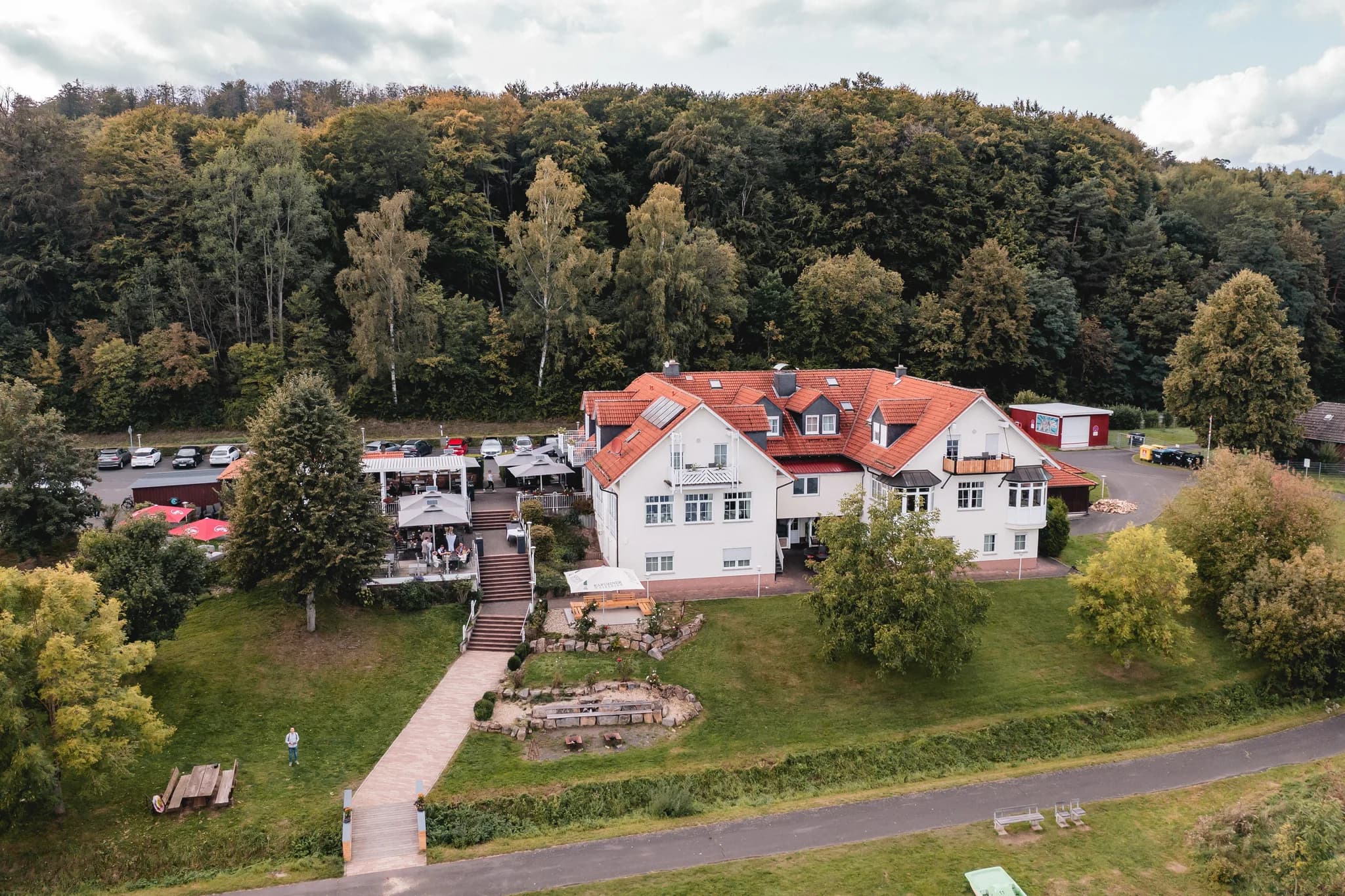 Drohnenansicht des Lakeside Resort Michaela mit dem weißen Hauptgebäude, der Terrasse und dem umliegenden Wald.