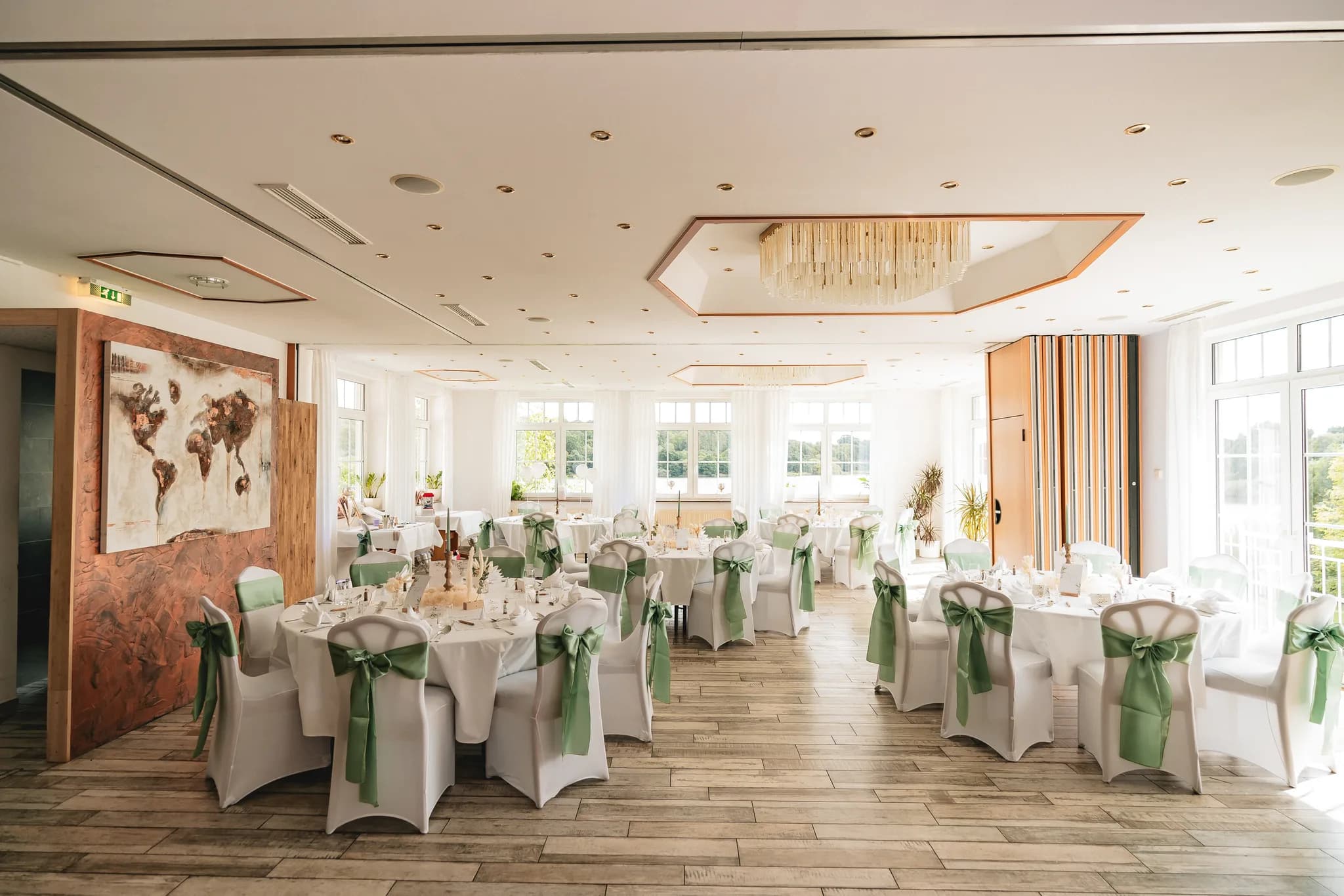Festlich gedeckte Tische mit weißen Tischdecken und grünen Stuhlschleifen im hellen Saal des Lakeside Resort Michaela.