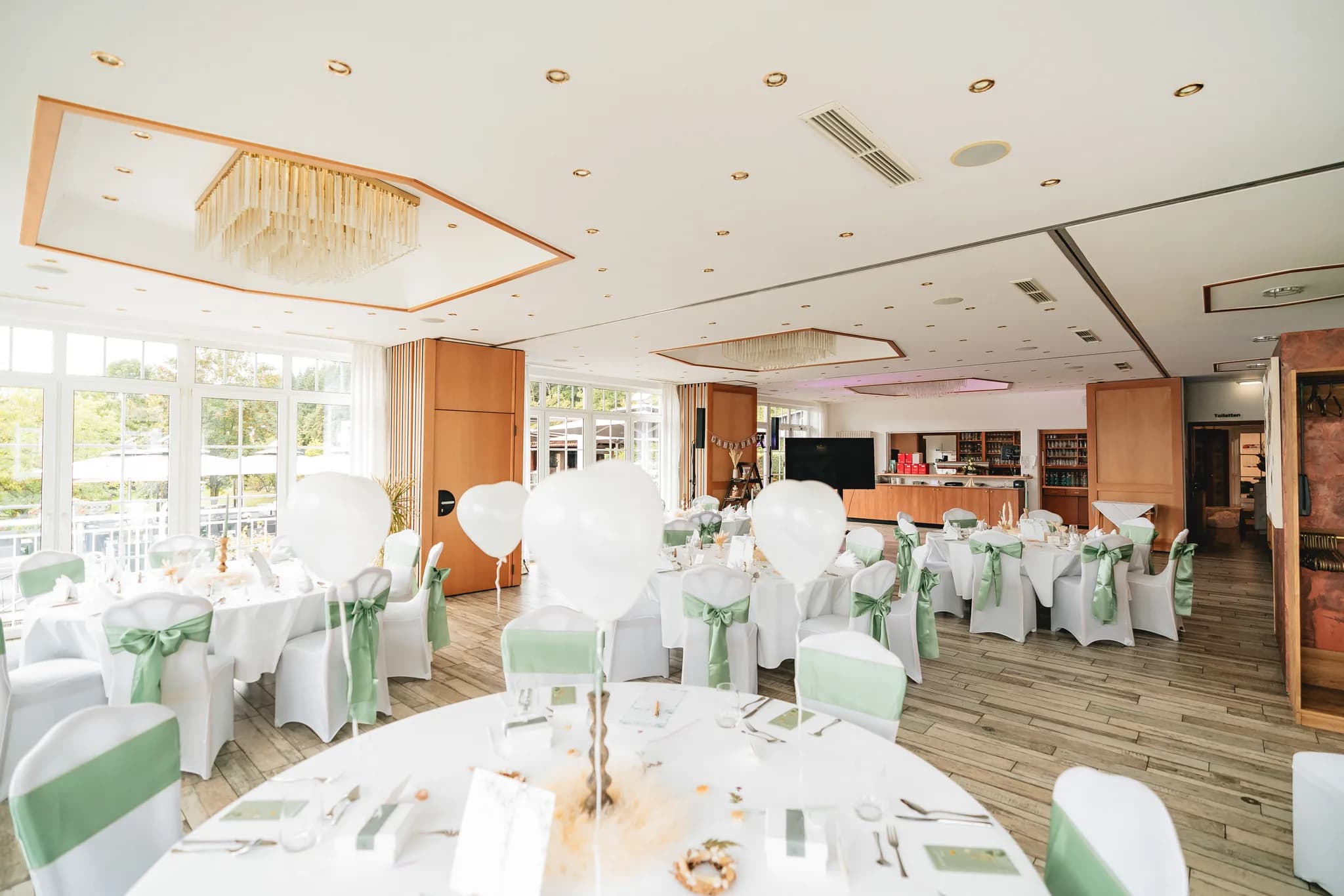 Festlich eingedeckter Hochzeitssaal im Lakeside Resort Michaela mit weißen Luftballons und mintgrünen Stuhlschleifen.