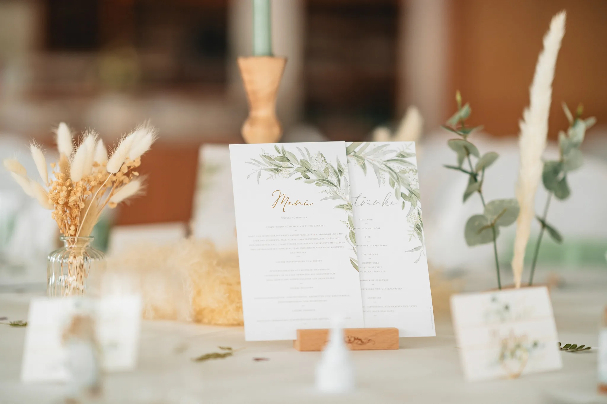Die Menü- und Getränkekarten mit zartem Eukalyptus-Design stehen stilvoll dekoriert auf einem Hochzeitstisch im Lakeside Resort.
