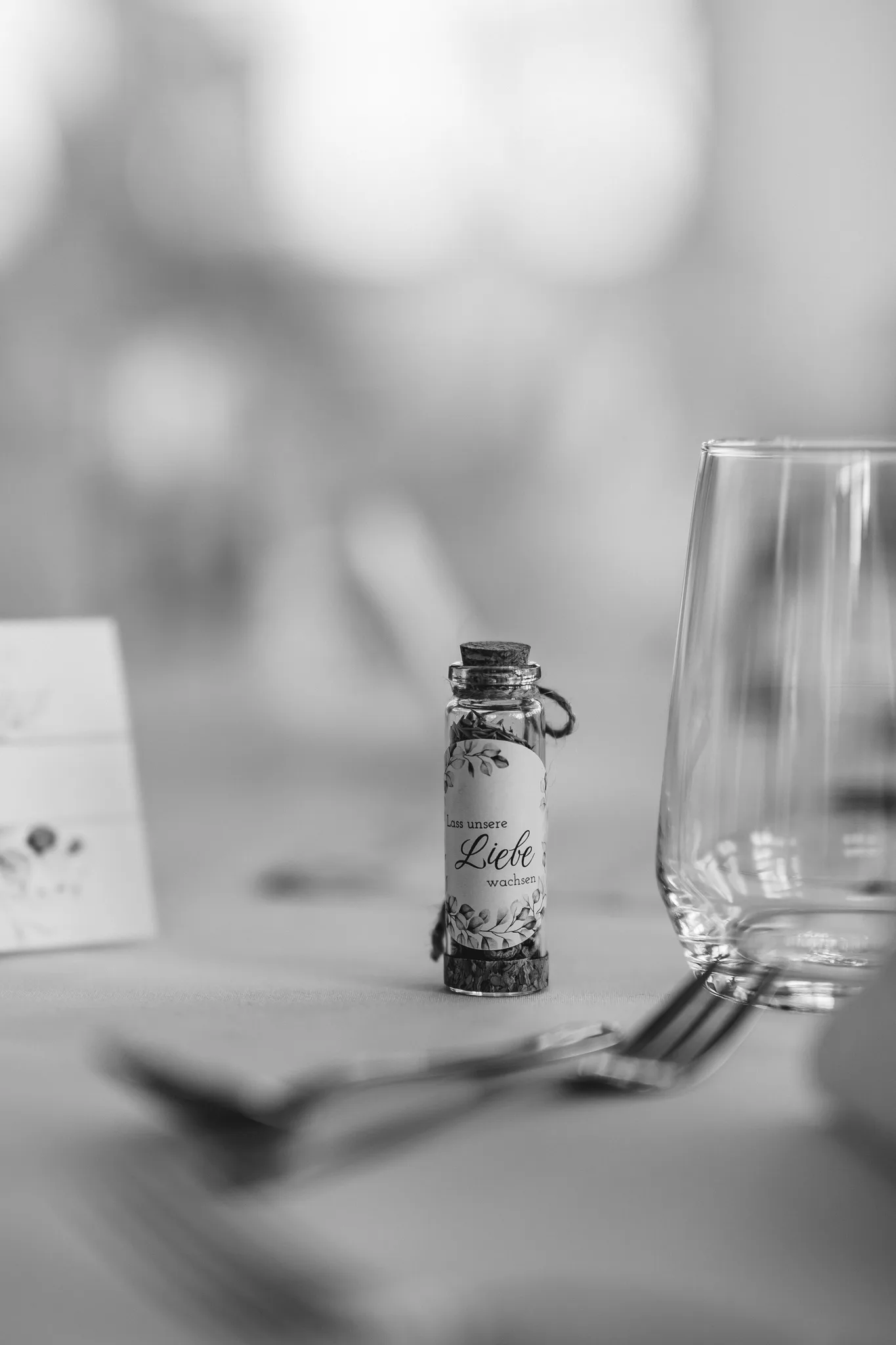 Kleines Fläschchen mit der Aufschrift Lass unsere Liebe wachsen als Gastgeschenk auf einem gedeckten Hochzeitstisch.