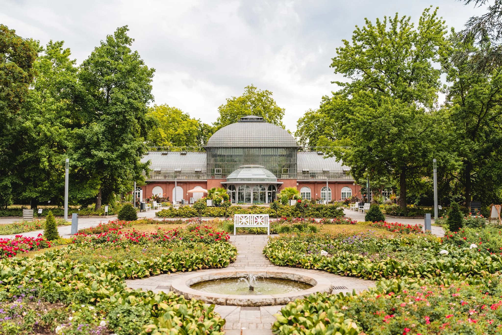 Blick auf das historische Gesellschaftshaus im Palmengarten Frankfurt mit seinem blühenden Garten und Springbrunnen.