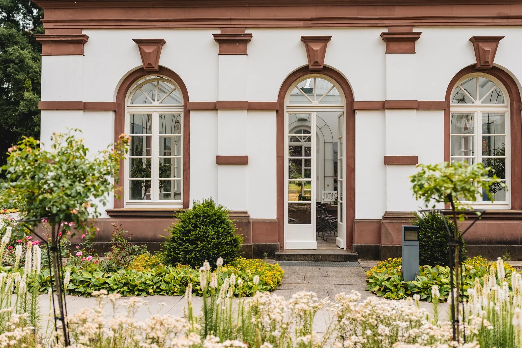 Die historische Fassade des Palmengartens Frankfurt mit ihren Rundbogenfenstern umgeben von einem blühenden Garten.