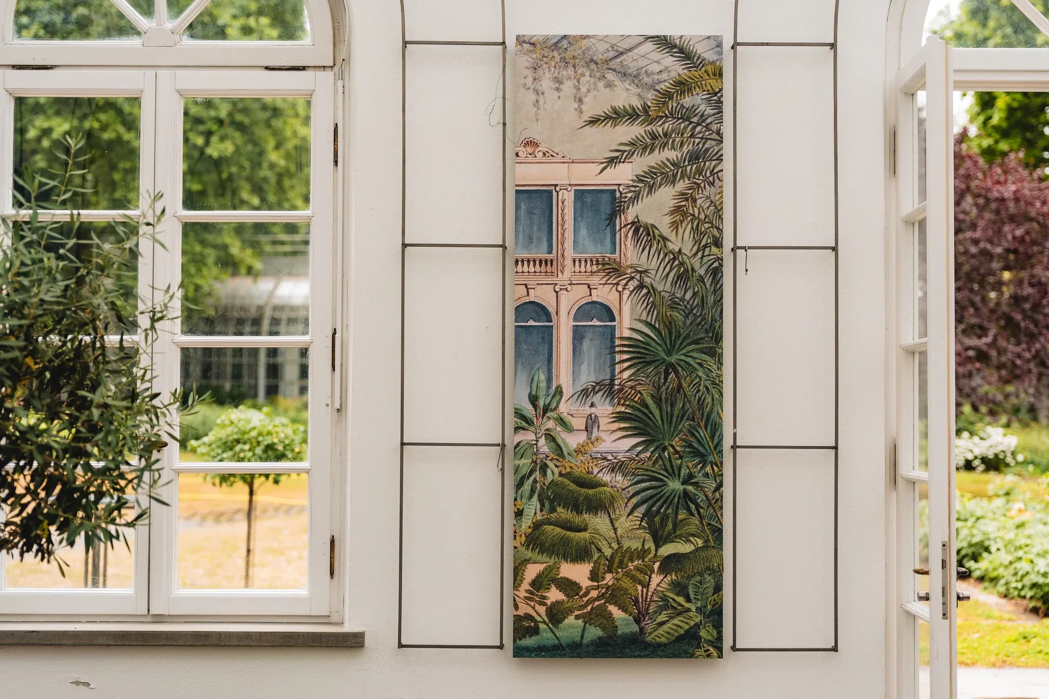 Ein historisches Wandgemälde mit Palmenmotiv zwischen zwei weißen Fenstern im Palmengarten Frankfurt.