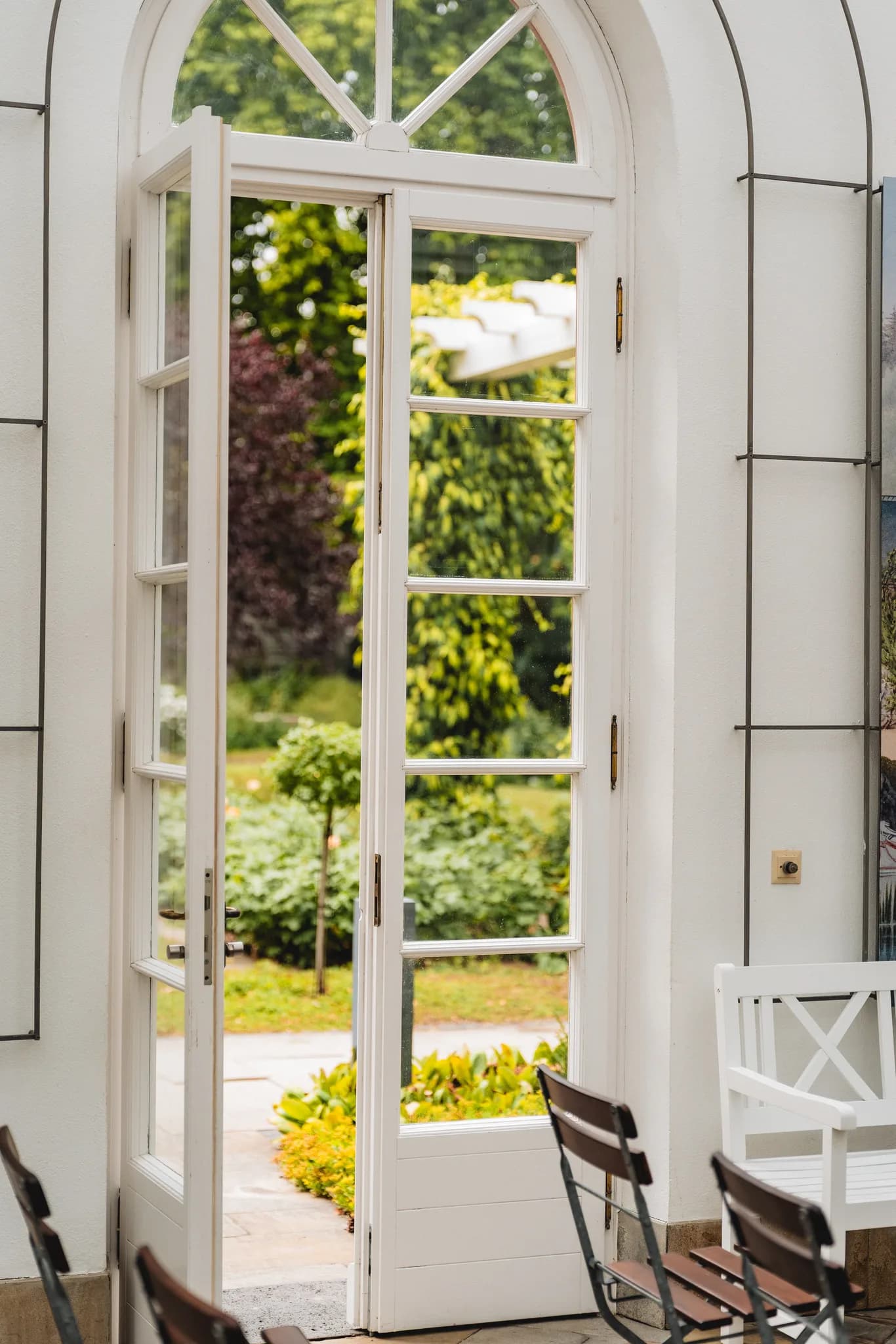 Blick durch die geöffnete Fenstertür einer hellen Räumlichkeit in den grünen Garten des Palmengartens Frankfurt.