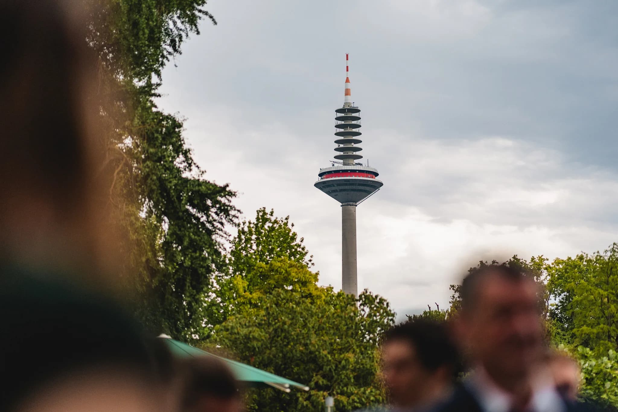 Der Frankfurter Fernsehturm ragt hinter den Bäumen im Palmengarten über einer Hochzeitsgesellschaft auf.