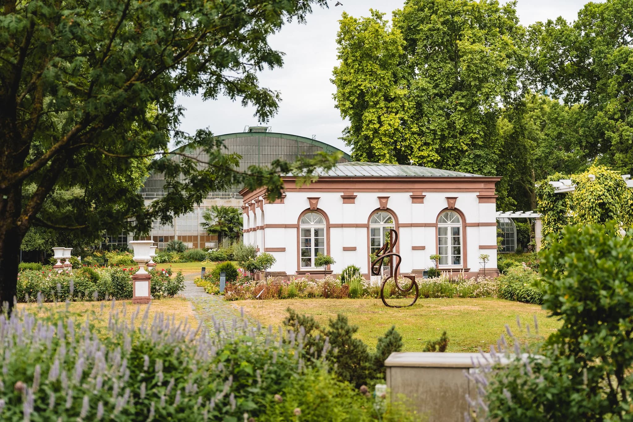 Historisches Gebäude im Palmengarten Frankfurt umgeben von üppig grünen Pflanzen und sommerlichen Blumenbeeten.