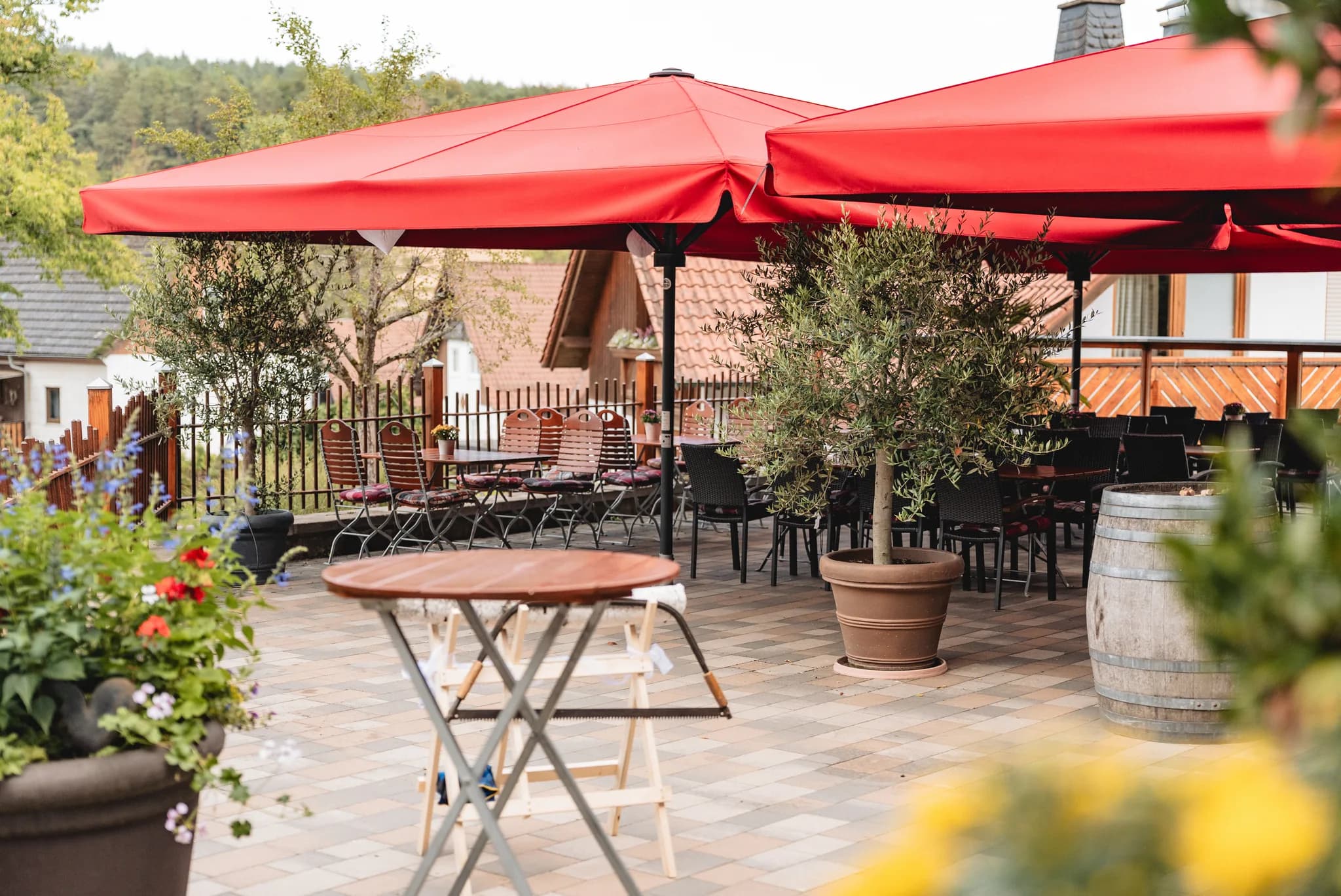 Gedeckte Terrasse in Kleinlüder mit roten Sonnenschirmen, Olivenbäumen und einem Holzsäge-Hindernis für Hochzeitsspiele.