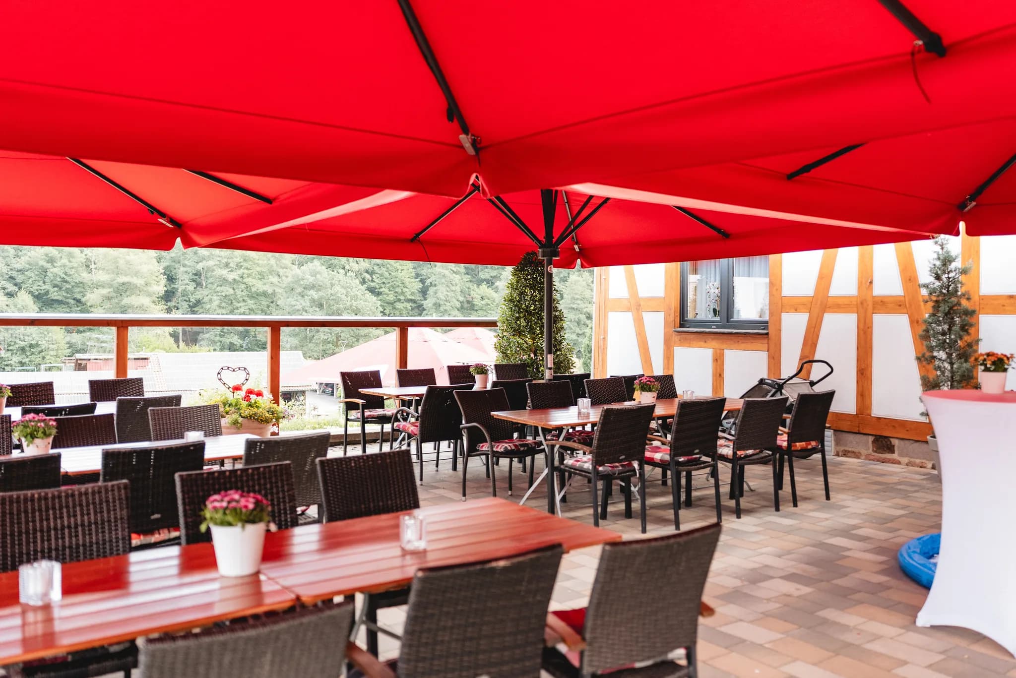 Gedeckte Tische unter einem großen roten Sonnenschirm auf einer Terrasse in Kleinlüder bei einer Hochzeitsfeier.