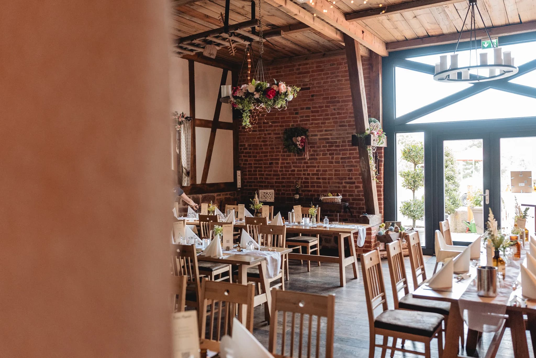Festlich eingedeckte Holztische in einer rustikalen Eventlocation mit Backsteinwänden und Blumenkranz in Kleinlüder.