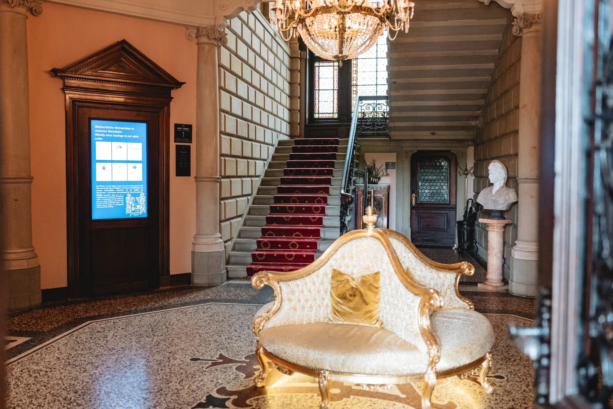 Prunkvolles Foyer mit rotem Treppenaufgang, goldenem Sofa und Büste in einem historischen Schloss in Lieser an der Mosel.
