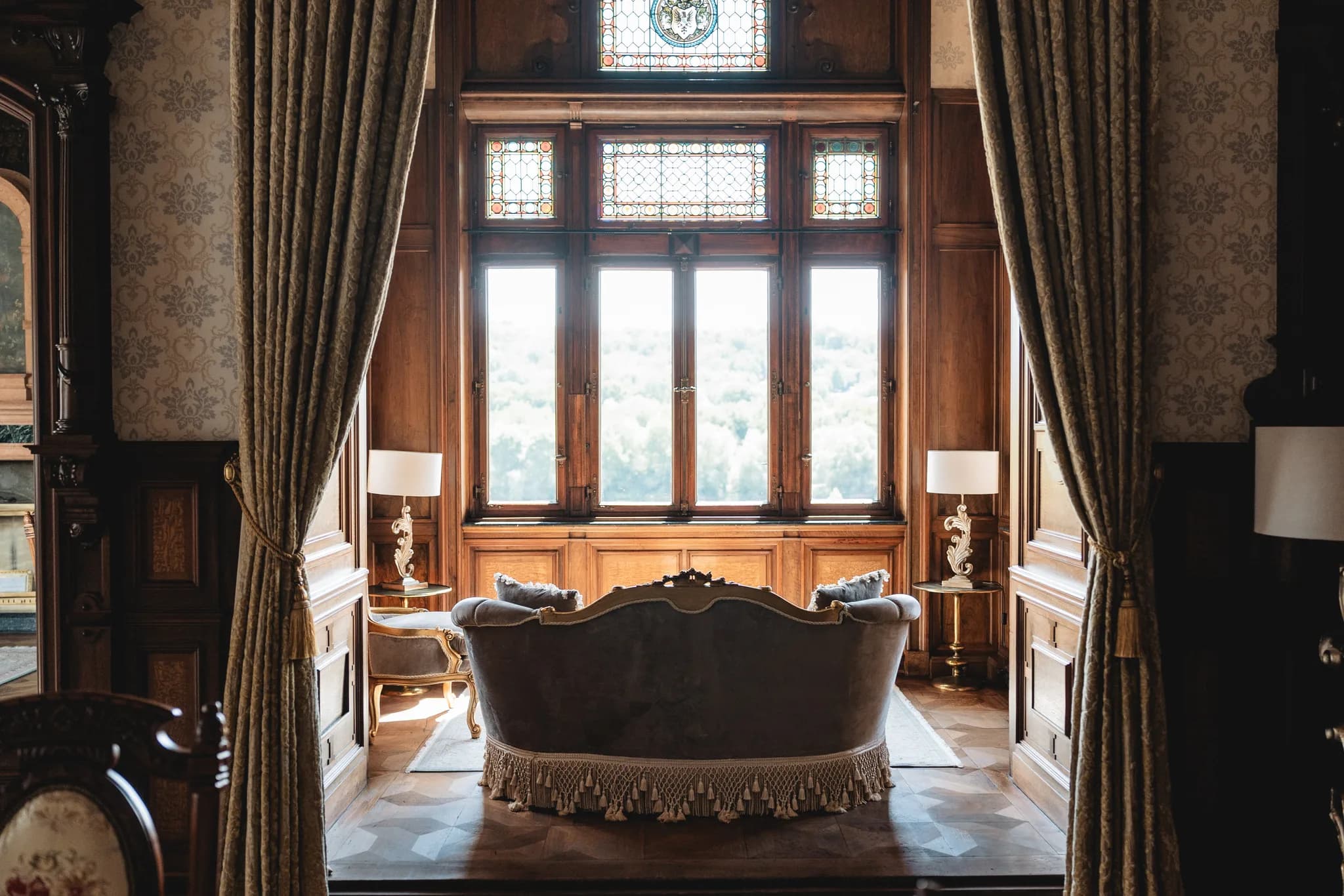 Elegantes historisches Interieur mit einem mit Quasten verzierten Sofa vor großen Fenstern in Lieser an der Mosel.