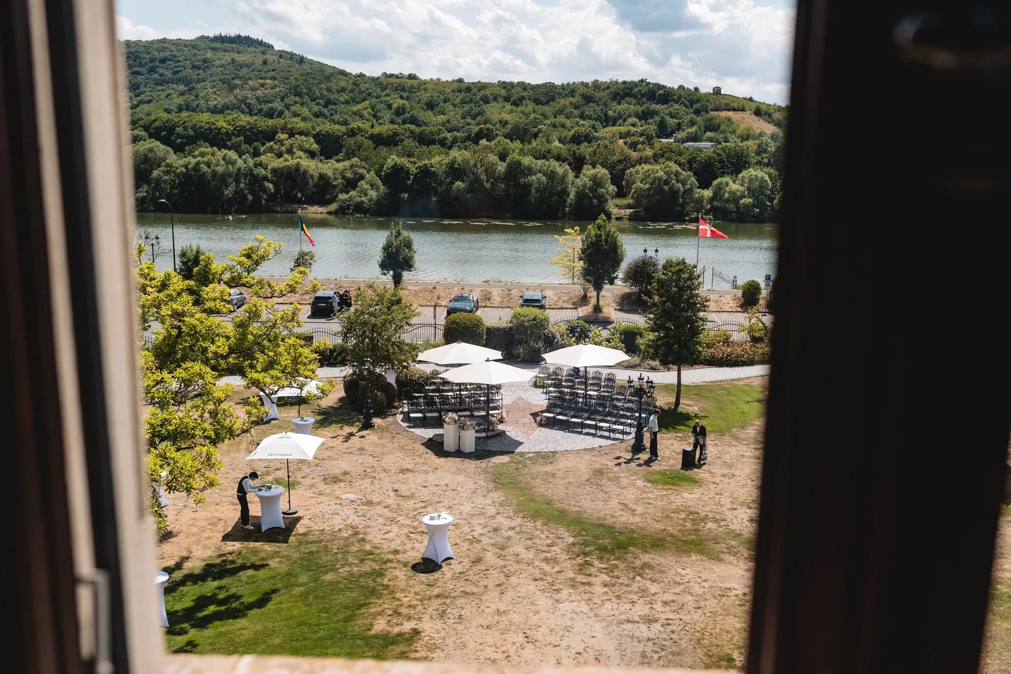 Blick aus einem Fenster auf die vorbereitete Hochzeitslocation am Moselufer in Lieser mit Stuhlreihen und Stehtischen.