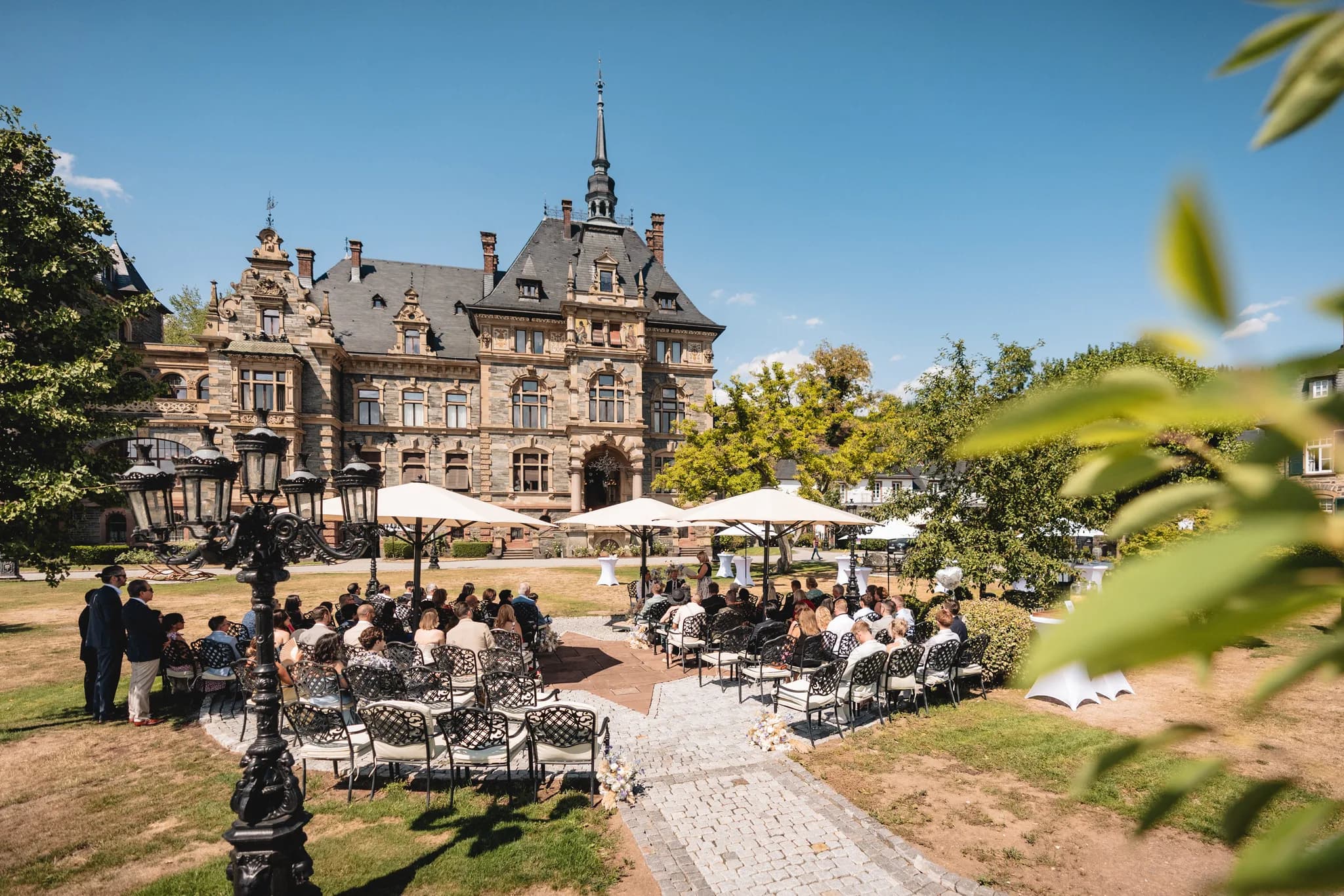 Hochzeitsgäste sitzen bei strahlendem Sonnenschein zur Trauung vor dem historischen Schloss Lieser an der Mosel.