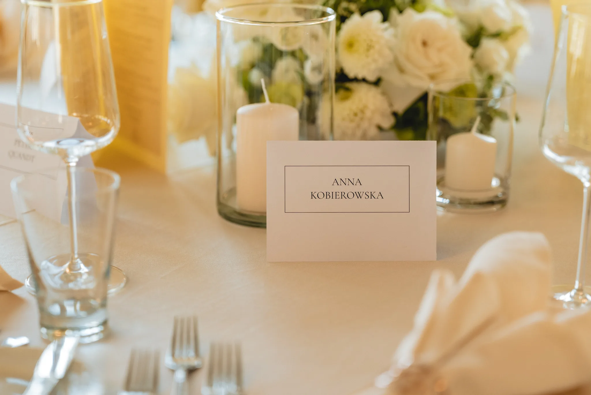 Elegantes Platzkärtchen für eine Hochzeit in Lieser an der Mosel mit weißem Blumenschmuck und Kerzen auf dem Tisch.