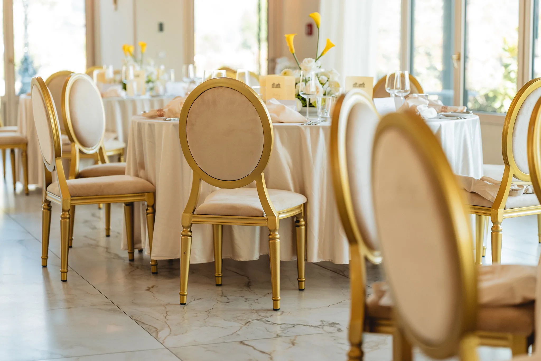 Festlich gedeckte runde Tische mit eleganten Goldstühlen in einem lichtdurchfluteten Saal in Lieser an der Mosel.