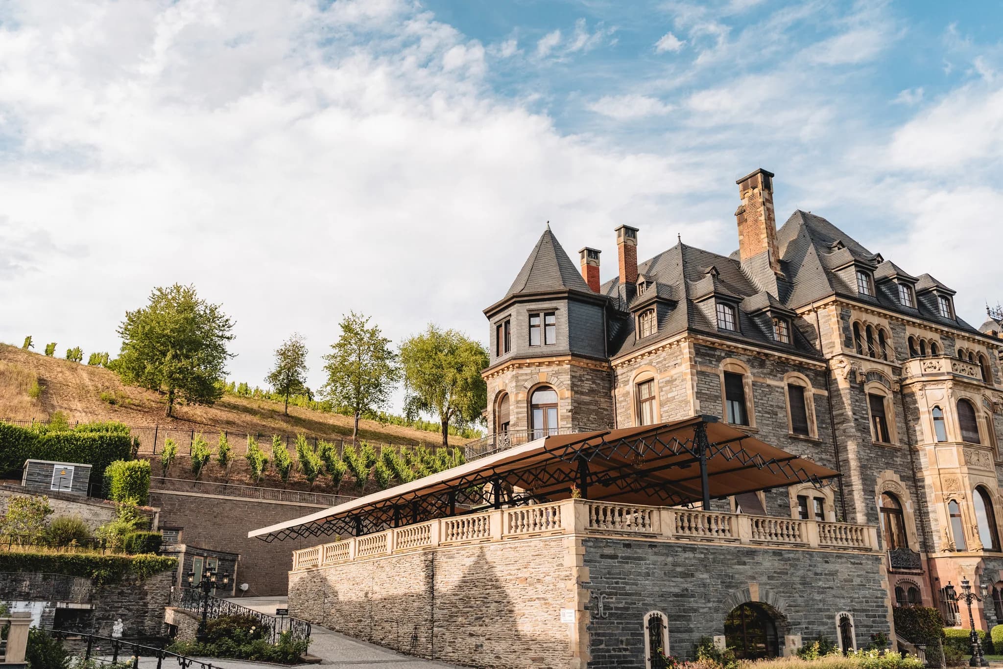 Die historische Fassade von Schloss Lieser an der Mosel mit der großen Terrasse vor den umliegenden Weinbergen.