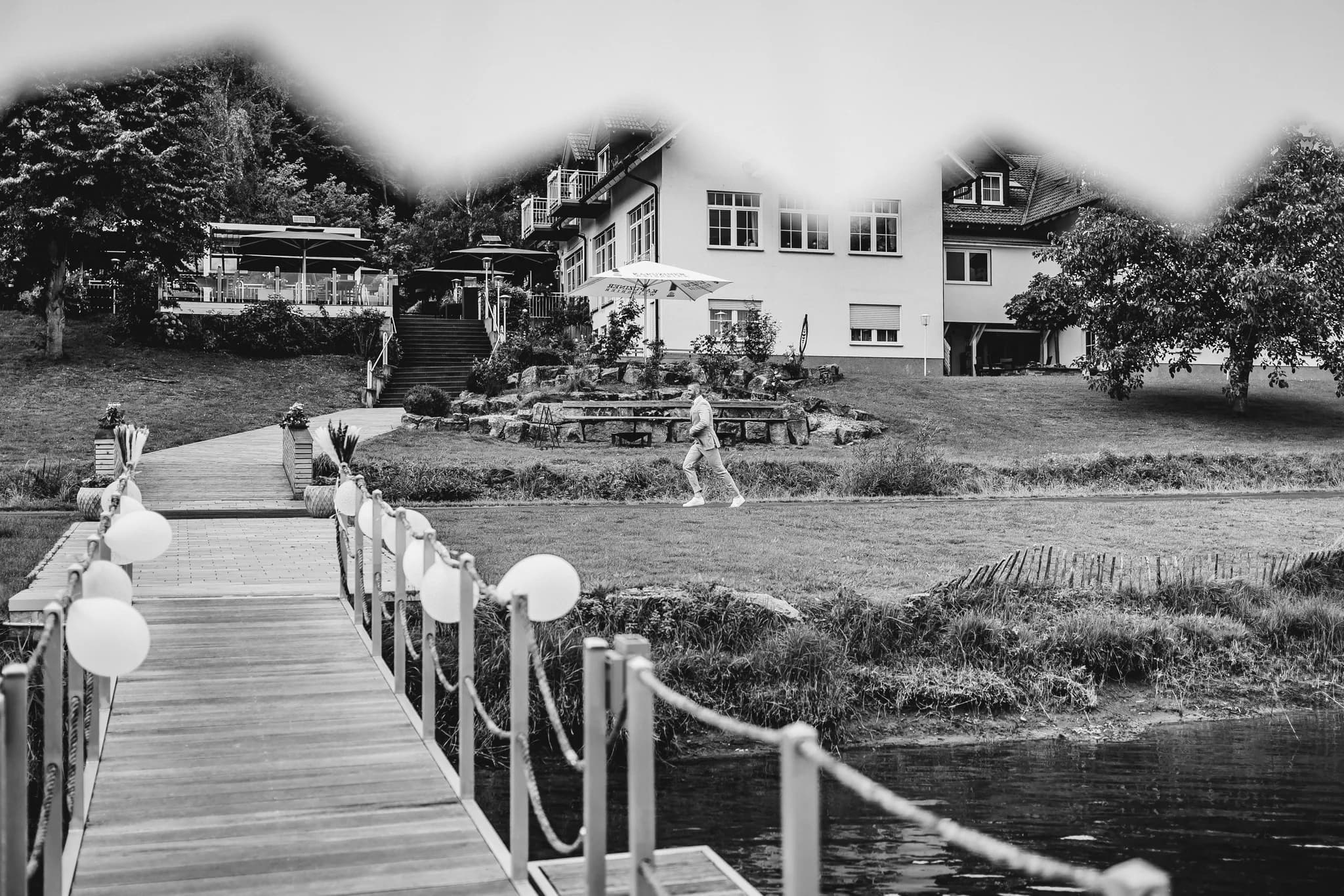 Daniel spaziert im hellen Anzug über das Gelände des Lakeside Resort Michaela vor dem geschmückten Holzsteg.