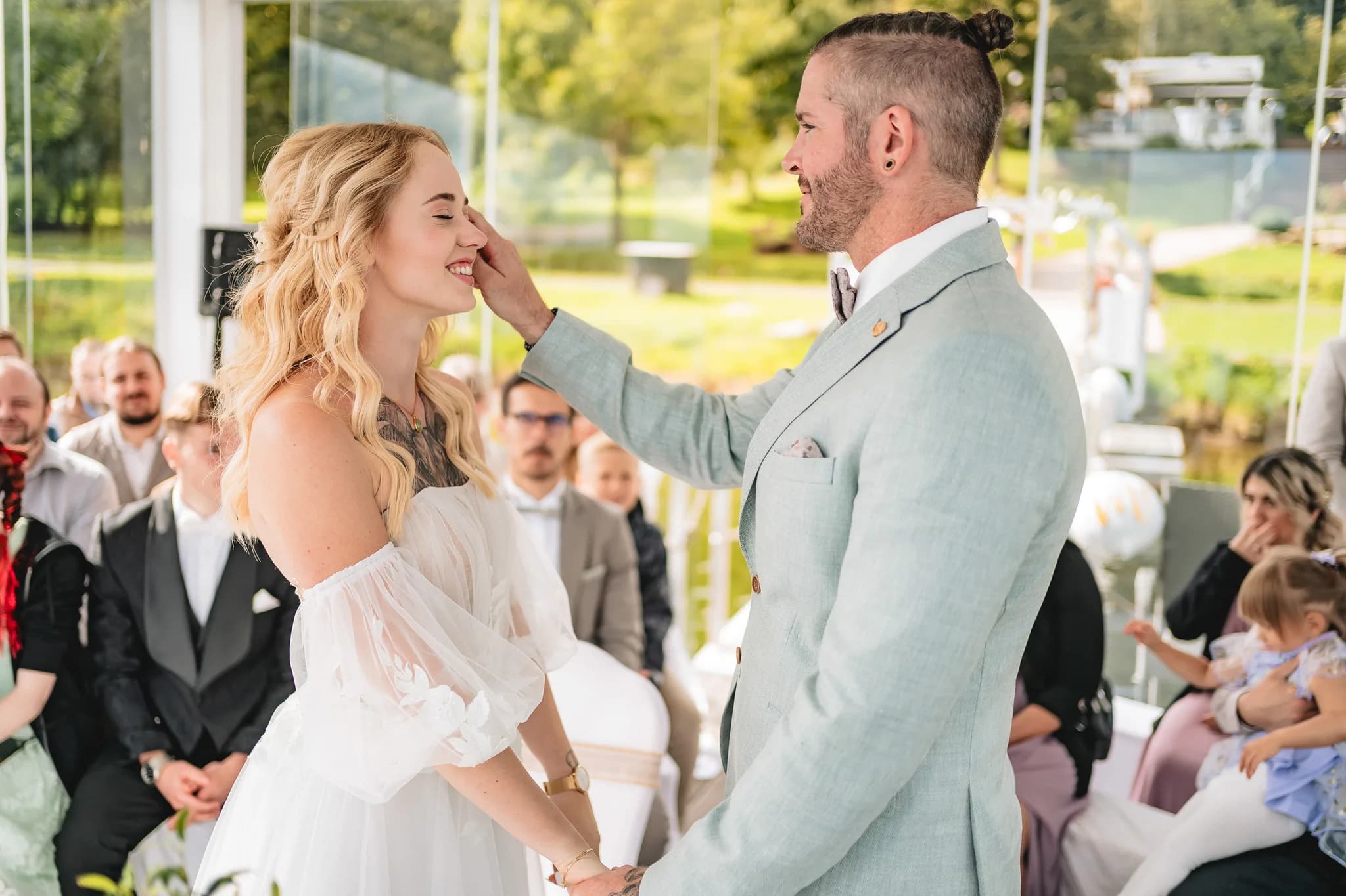 Daniel streicht seiner Braut Peggy während der Trauung im Lakeside Resort Michaela liebevoll über das Gesicht.