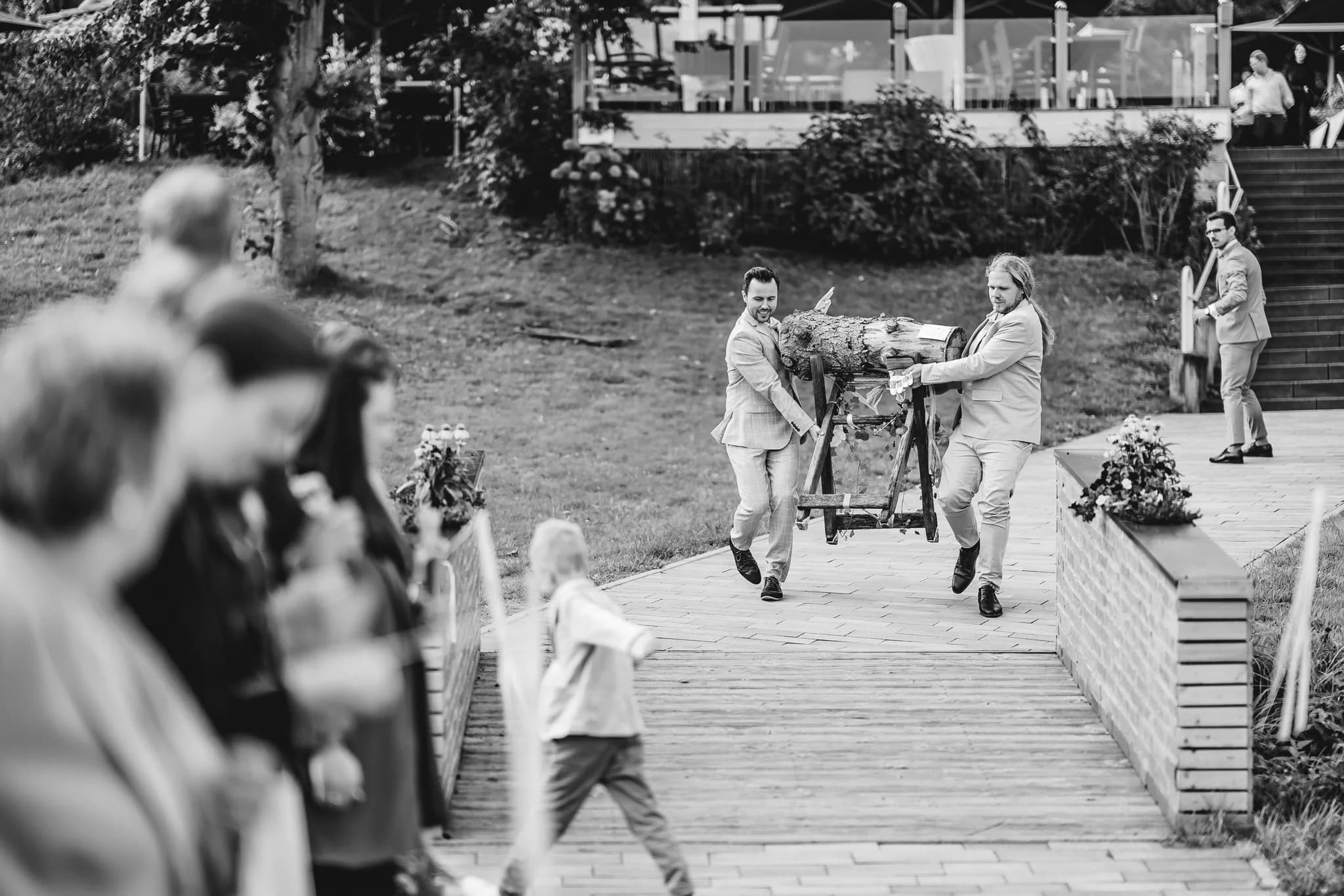 Zwei Männer tragen bei der Hochzeit von Peggy und Daniel einen Baumstamm zum Sägen ins Lakeside Resort Michaela.