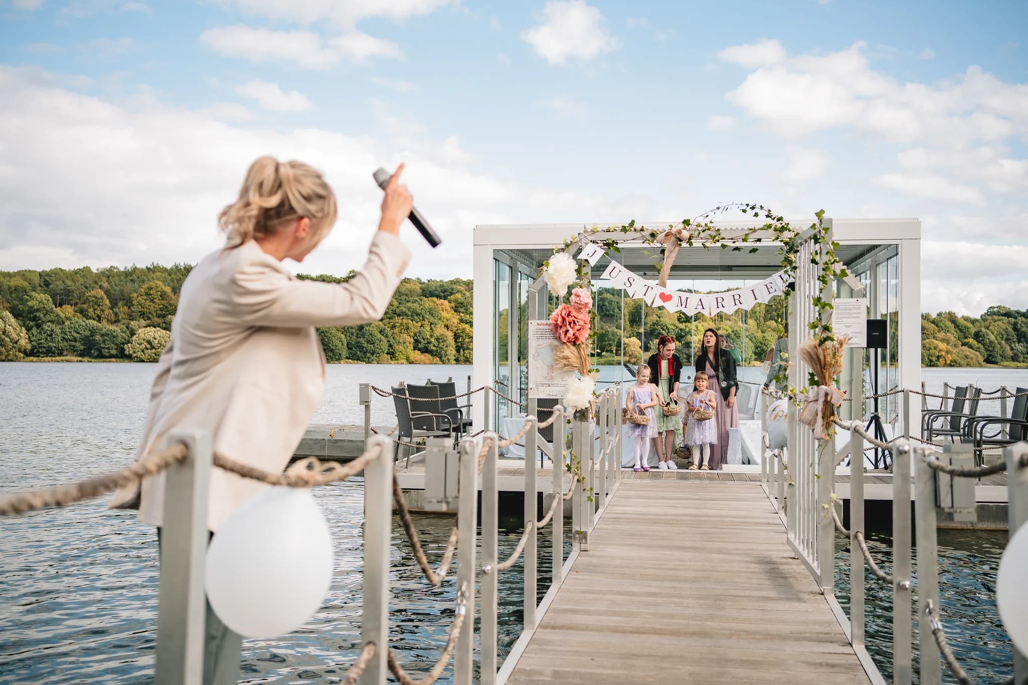 Eine Frau mit Mikrofon moderiert die Zeremonie von Peggy und Daniel vor dem geschmückten Pavillon im Lakeside Resort.