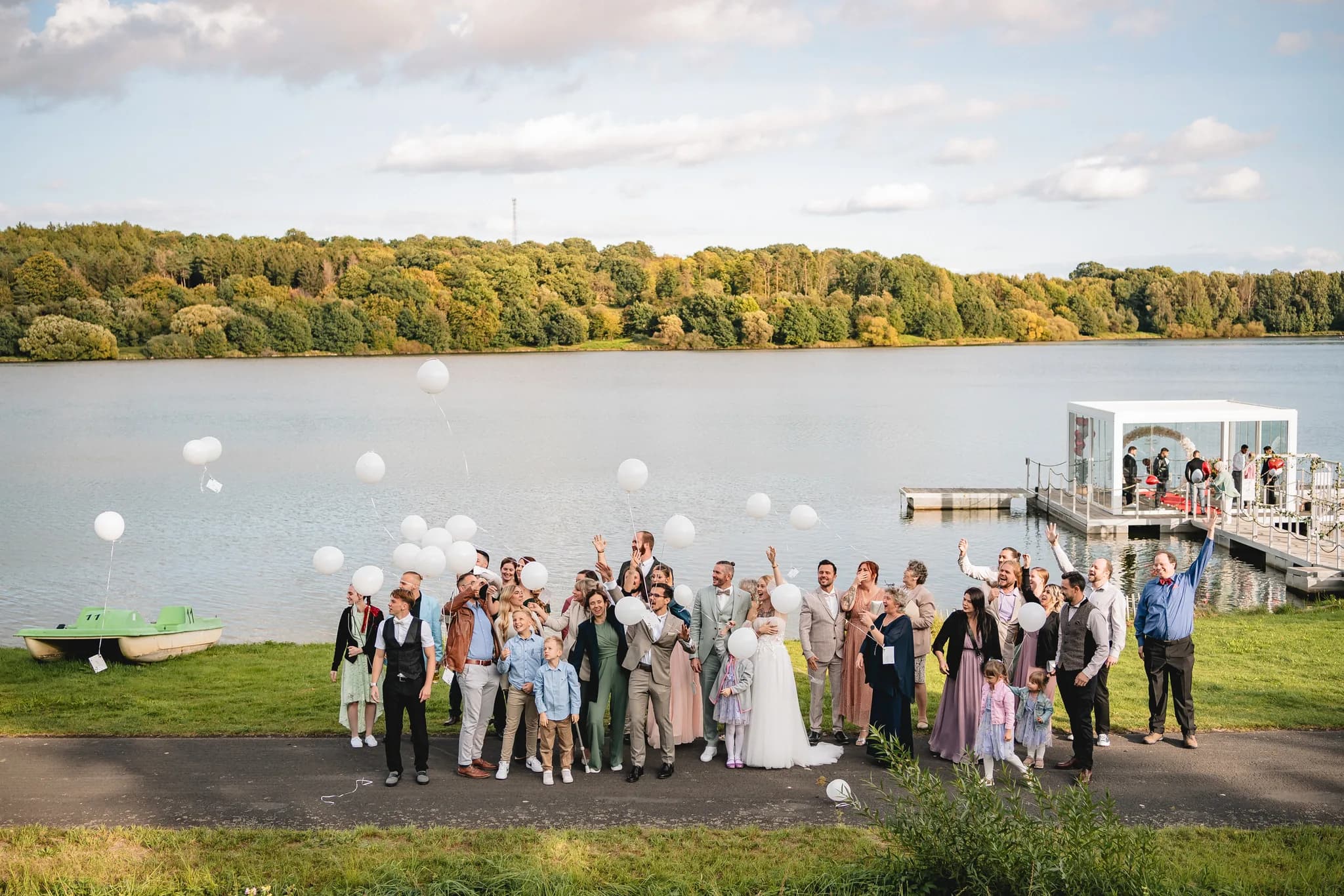 Hochzeitsgesellschaft lässt am Seeufer des Lakeside Resorts Michaela gemeinsam weiße Luftballons in den Himmel steigen.