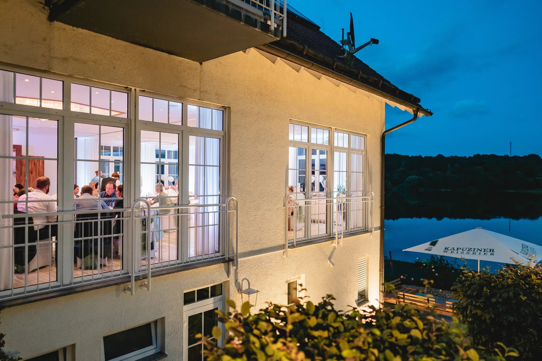 Hochzeitsgesellschaft von Peggy und Daniel feiert abends in den hell erleuchteten Räumlichkeiten des Lakeside Resorts.