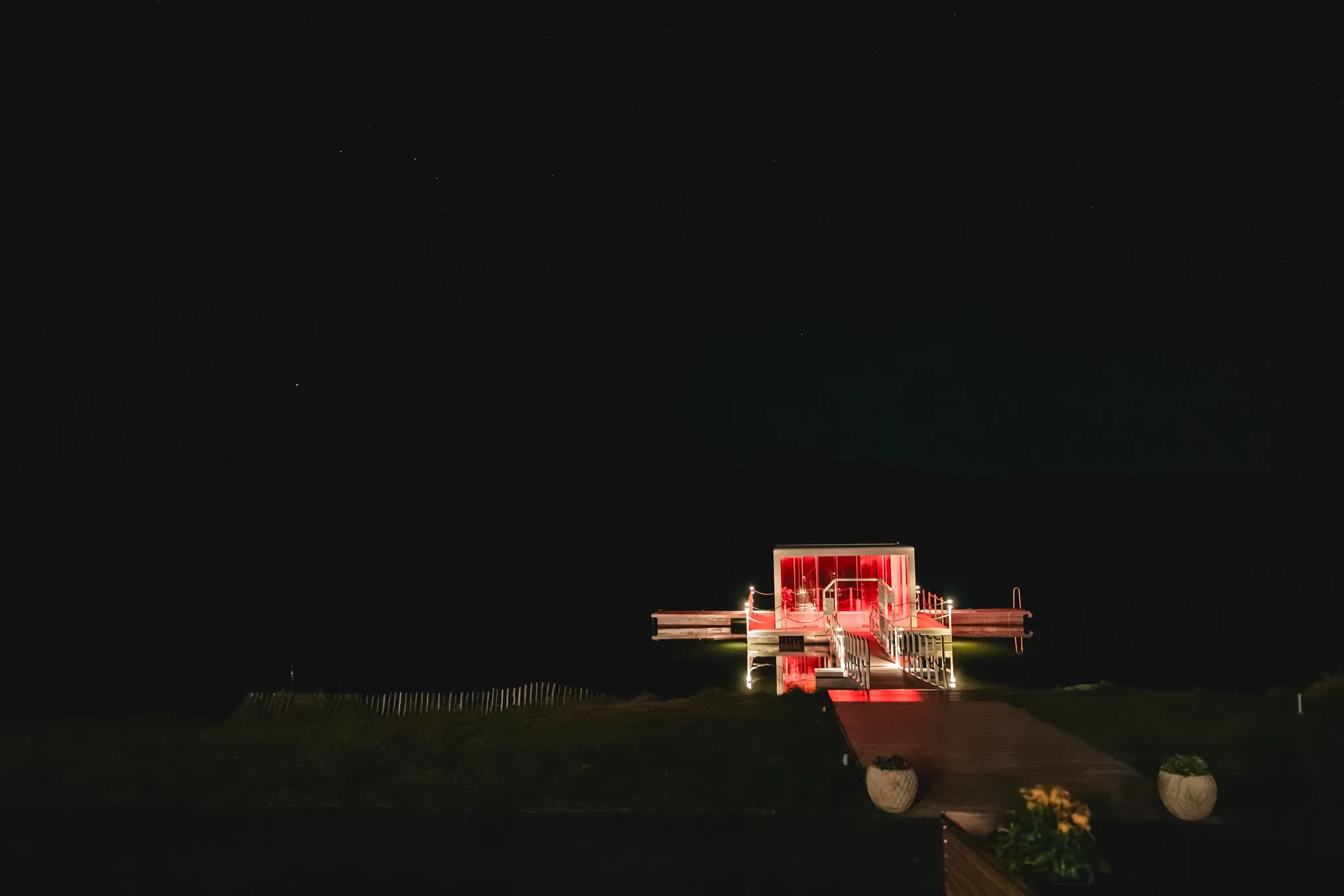 Stimmungsvolle nächtliche Ansicht des rot beleuchteten Stegs am Lakeside Resort Michaela während der Hochzeit von Peggy.