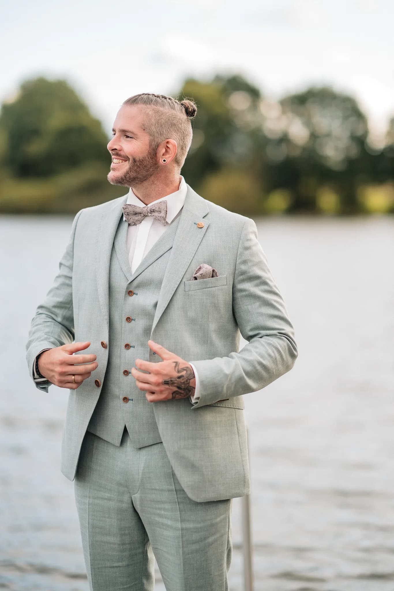 Daniel strahlt in seinem hellgrauen Hochzeitsanzug am Lakeside Resort Michaela glücklich in die Ferne.